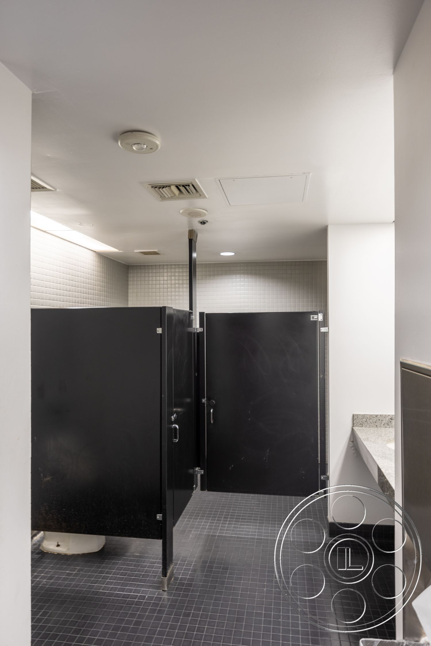 Rooftop 53 - white painted walls, drop ceiling with recessed lighting, modern restroom design, dark tile flooring, granite countertop sink area, interior restroom space, black laminate bathroom stall partitions, tile wall treatment