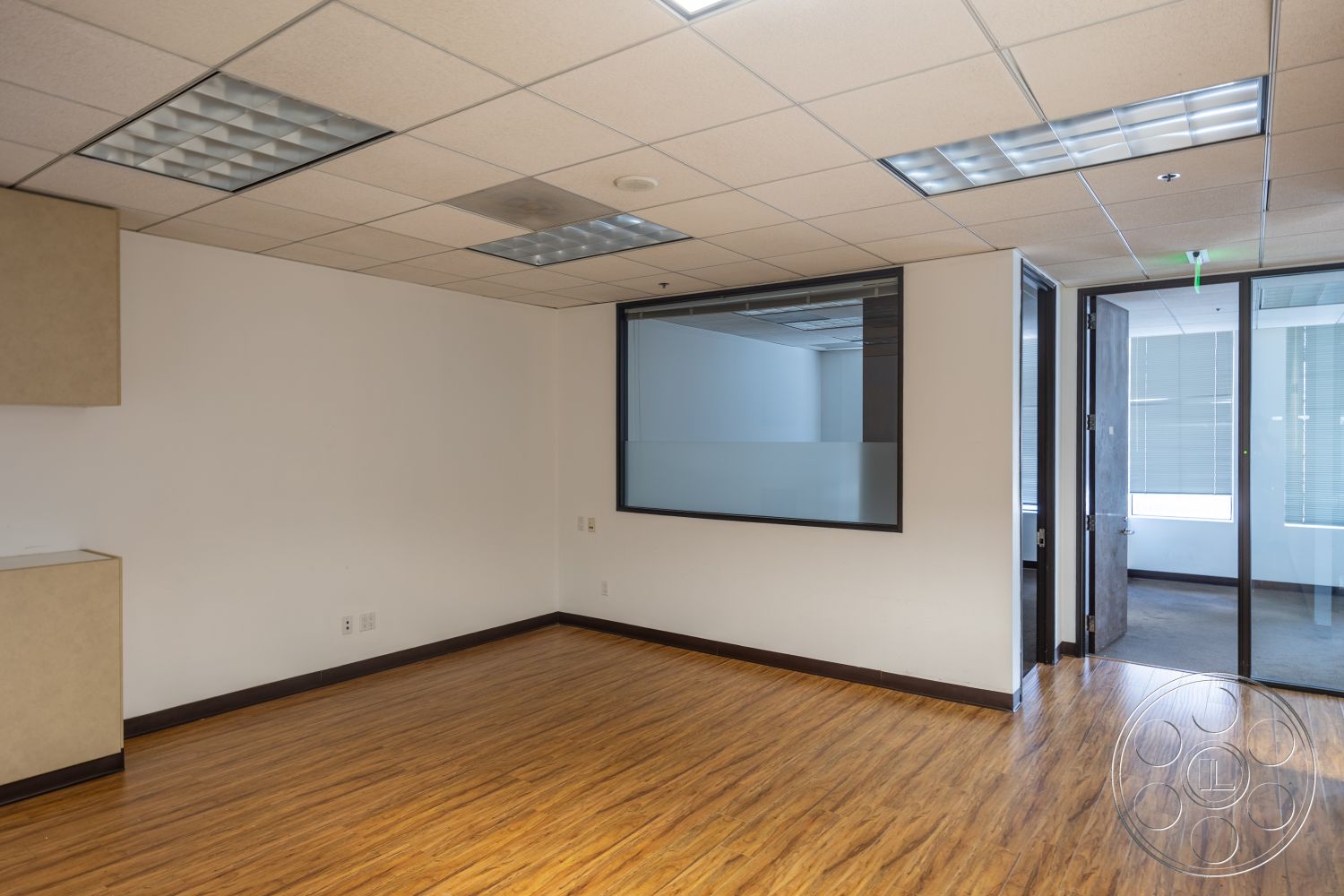 Rooftop 53 - glass door, light brown cabinetry, laminate wood flooring, glass partition wall, flat ceiling with fluorescent lighting, drywall painted white walls, office room layout