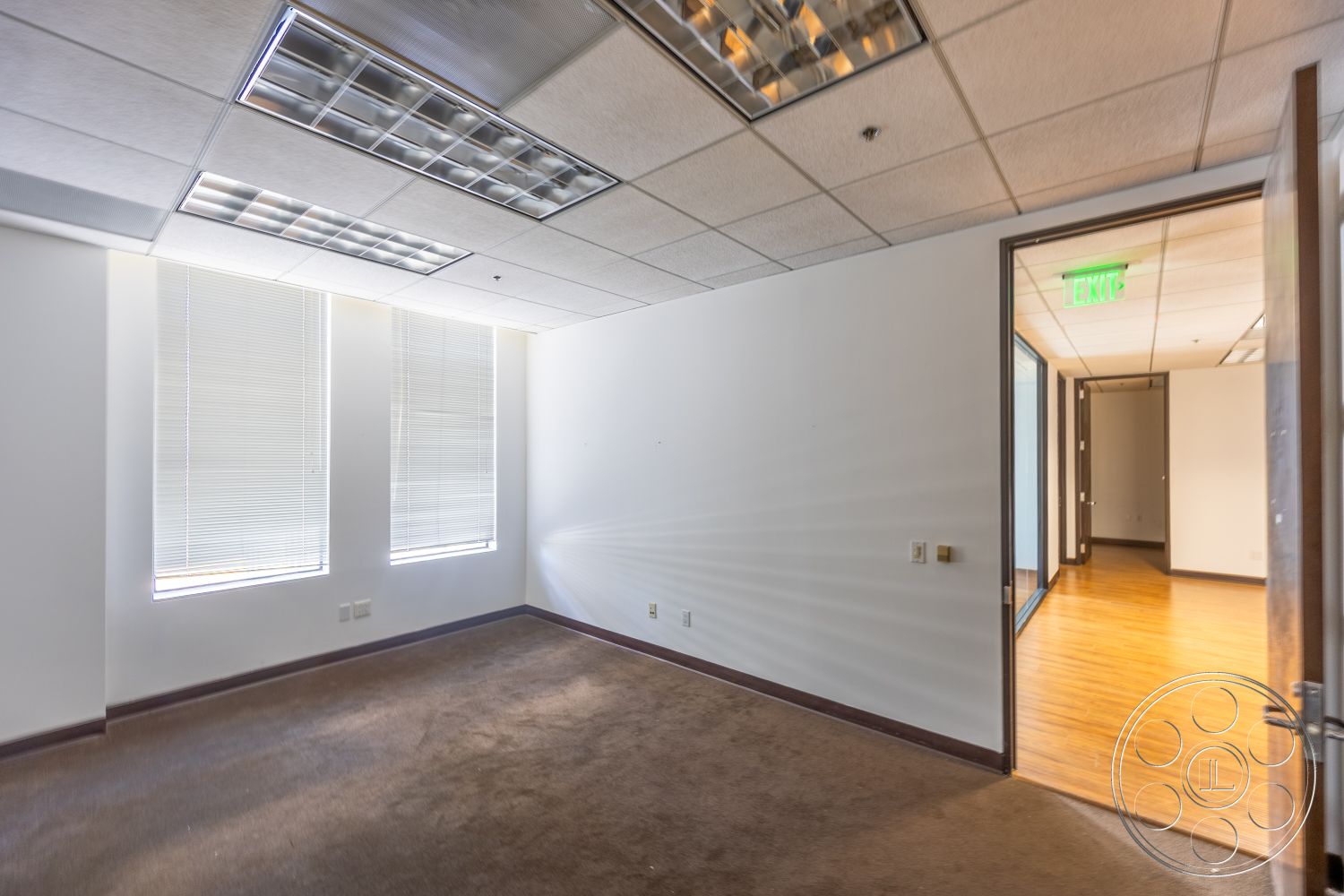 Rooftop 53 - neutral color palette, carpet flooring, office space, white painted walls, linear ceiling lights, wood trim details, glass windows with blinds, standard acoustic tile ceiling, doorway to exit