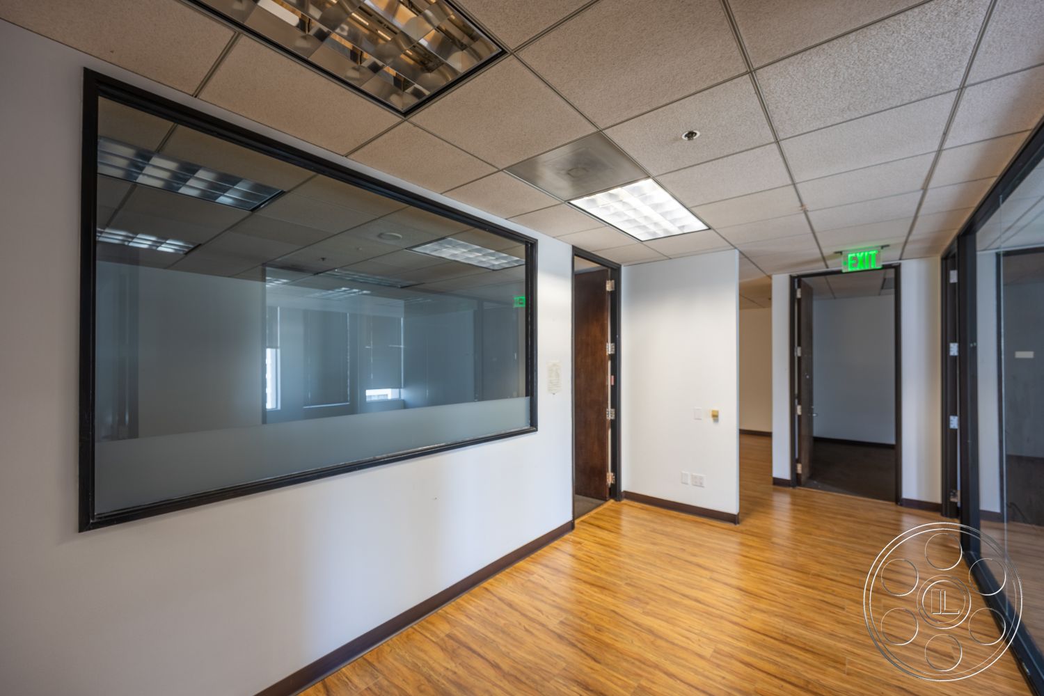 Rooftop 53 - textured wall finish, exit sign, open office space, wood laminate flooring, modern office layout, glass partition wall, drop ceiling with fluorescent lights, dark wood door frames