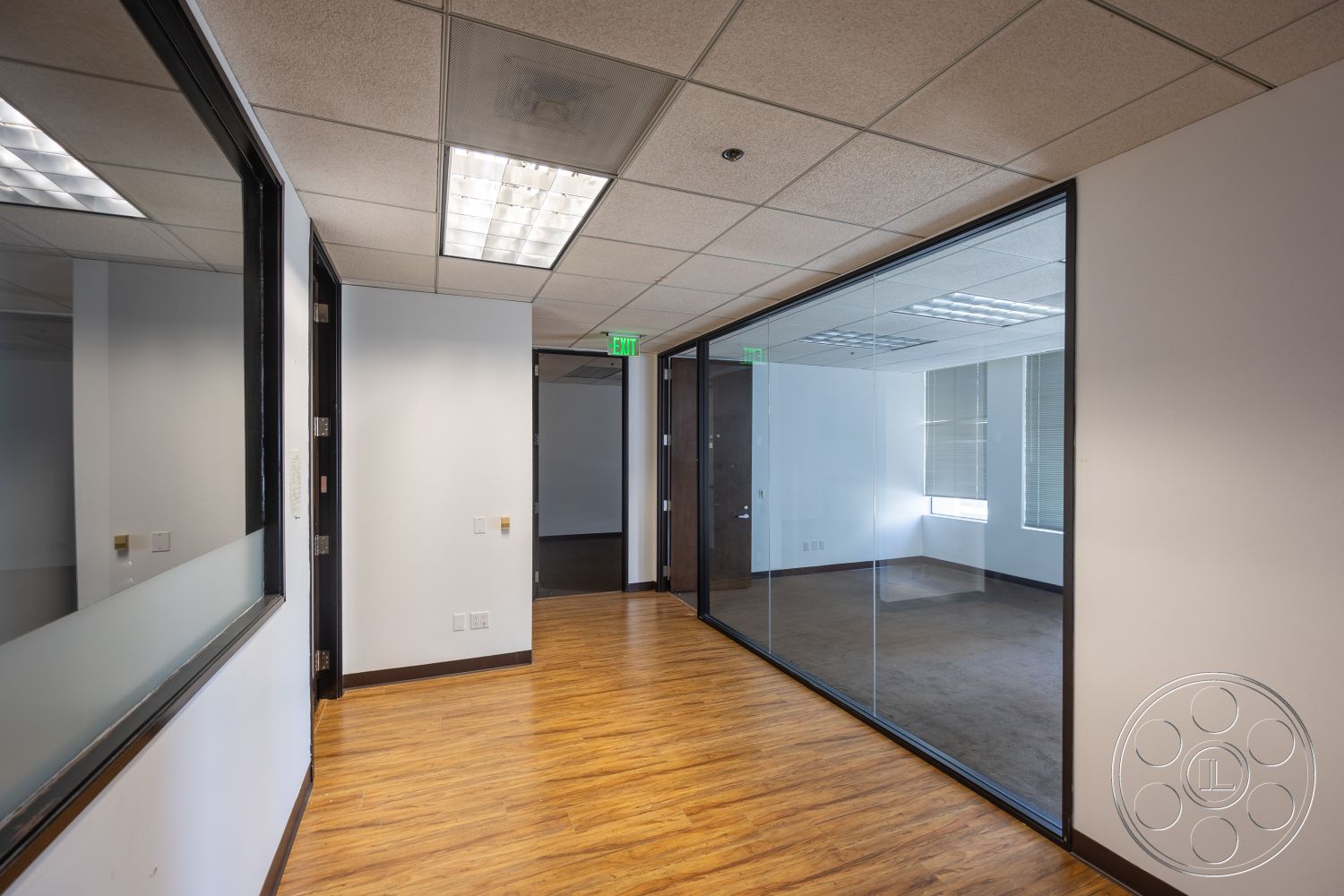 Rooftop 53 - dark wood doors, window blinds, laminate wood flooring, acoustic ceiling tiles, glass partition walls, white painted walls, rectangular office layout, fluorescent ceiling lights, office hallway
