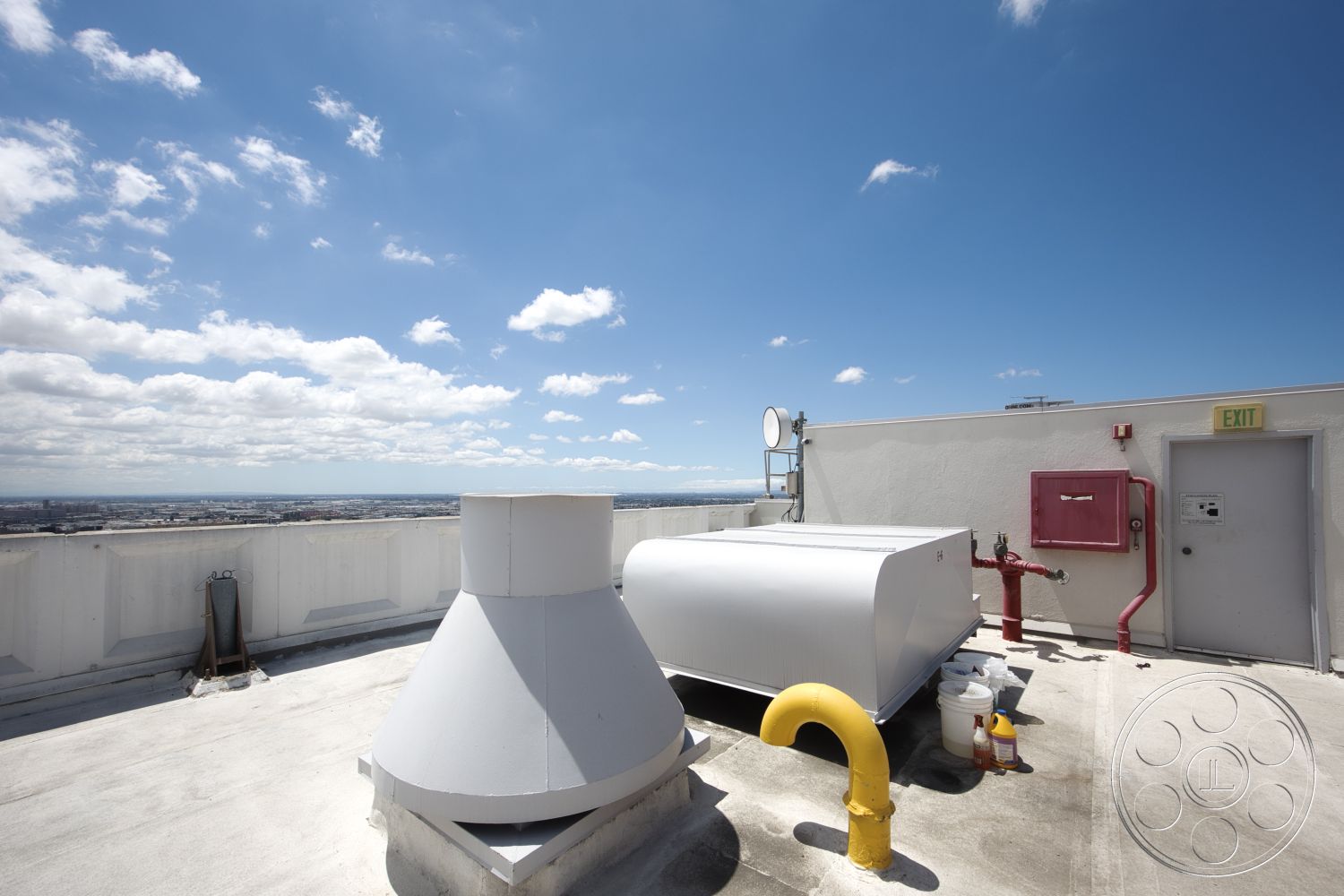 Rooftop 53 - open sky view, urban skyline backdrop, concrete structural walls, white flat roof surface, metal exhaust vents, industrial rooftop equipment, weatherproof antenna, red fire hose cabinet, yellow metal pipe, door access point, exterior rooftop setting