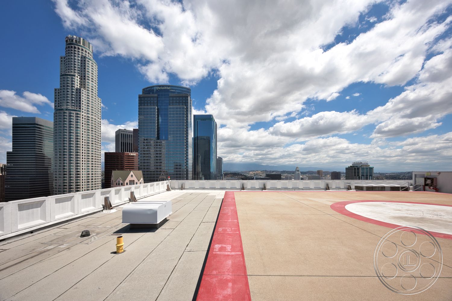 Rooftop 53 - exterior, steel railing, urban rooftop, city skyline view, flat roof design, concrete rooftop surface, modern high-rise buildings, red painted helicopter landing pad, sky with scattered clouds