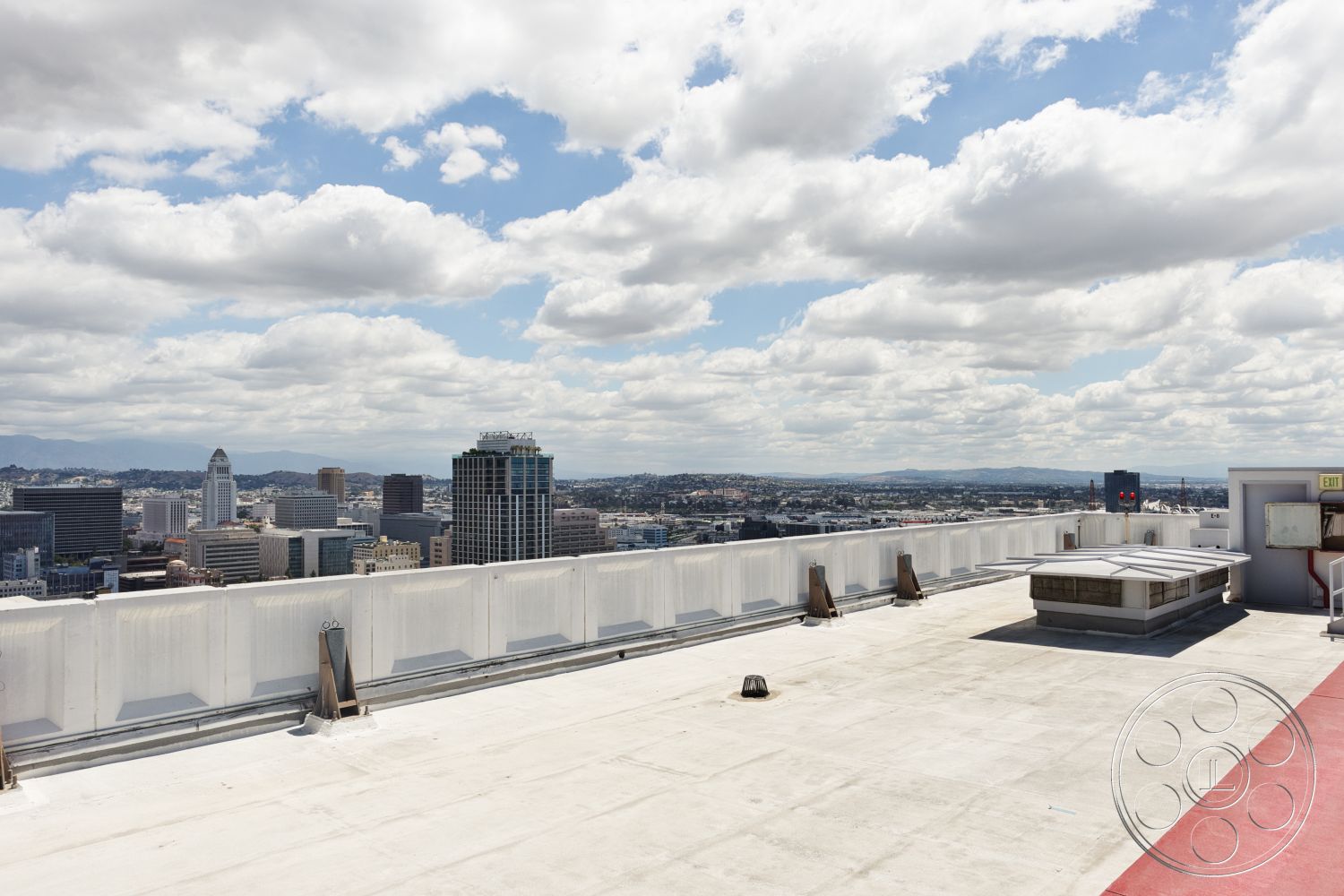 Rooftop 53 - exterior, flat roof, urban setting, city skyline view, white concrete walls, cloudy sky, metal railing details, concrete rooftop surface, HVAC units, domed skylight, rooftop access door