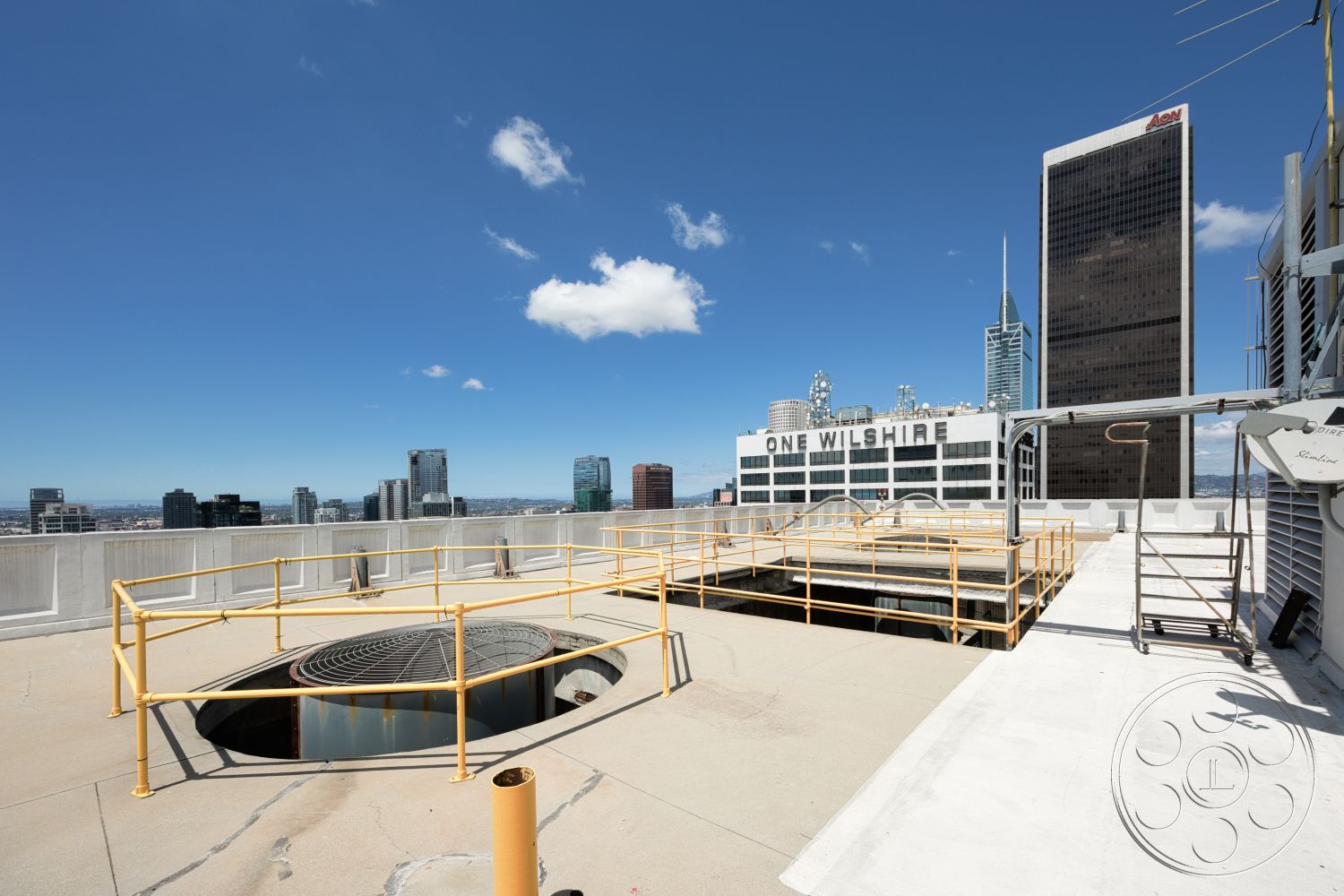 Rooftop 53 - exterior, urban skyline view, industrial equipment, flat roof design, metal safety railing, commercial building setting, concrete rooftop surface, circular ventilation shaft opening, yellow painted railings, high-rise structures in background