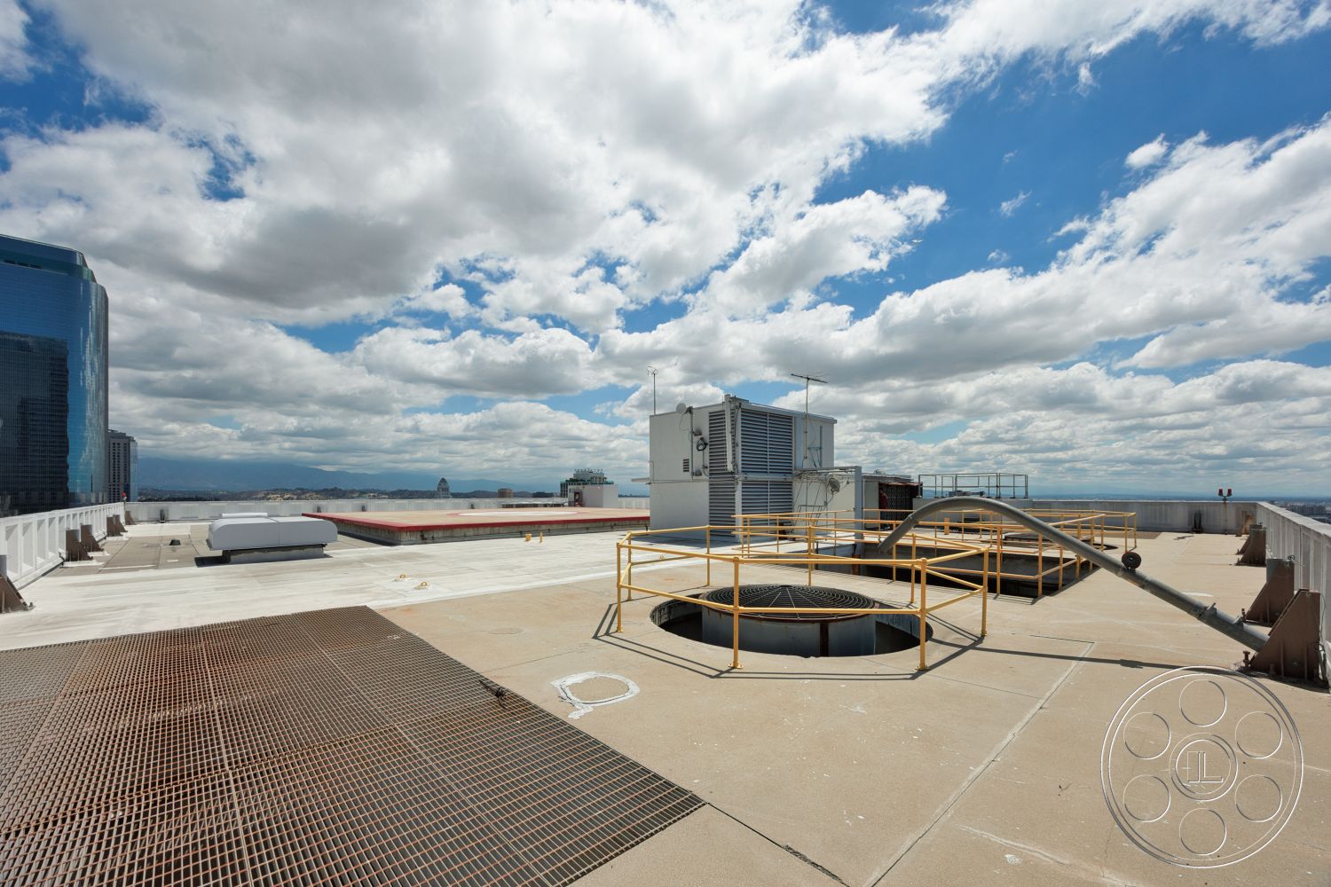 Rooftop 53 - exterior, city skyline view, concrete roof surface, flat roof surface, roof deck, metal grate flooring, industrial HVAC units, yellow safety railing, circular ventilation opening
