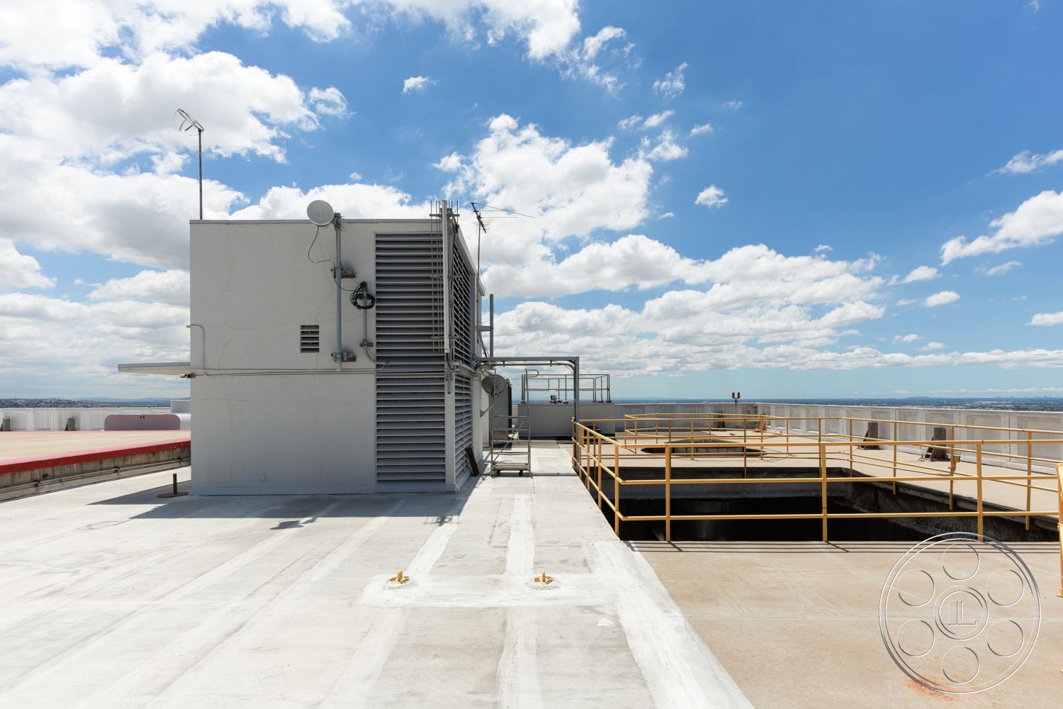 Rooftop 53 - exterior, metal railing, gray concrete walls, open sky view, concrete rooftop floor, flat roof surface, yellow safety railing, industrial ventilation unit, rectangular rooftop structure, mechanical equipment housing, white painted structural elements
