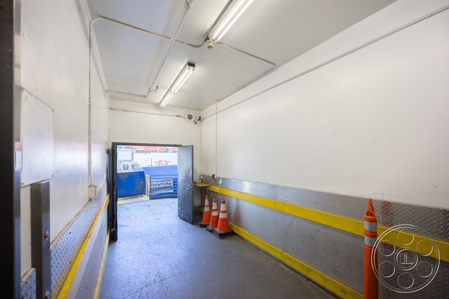 Rooftop 53 - interior hallway, white painted walls, LED ceiling lights, exposed concrete flooring, yellow safety line, metallic diamond plate wainscoting, double door entryway, traffic cones