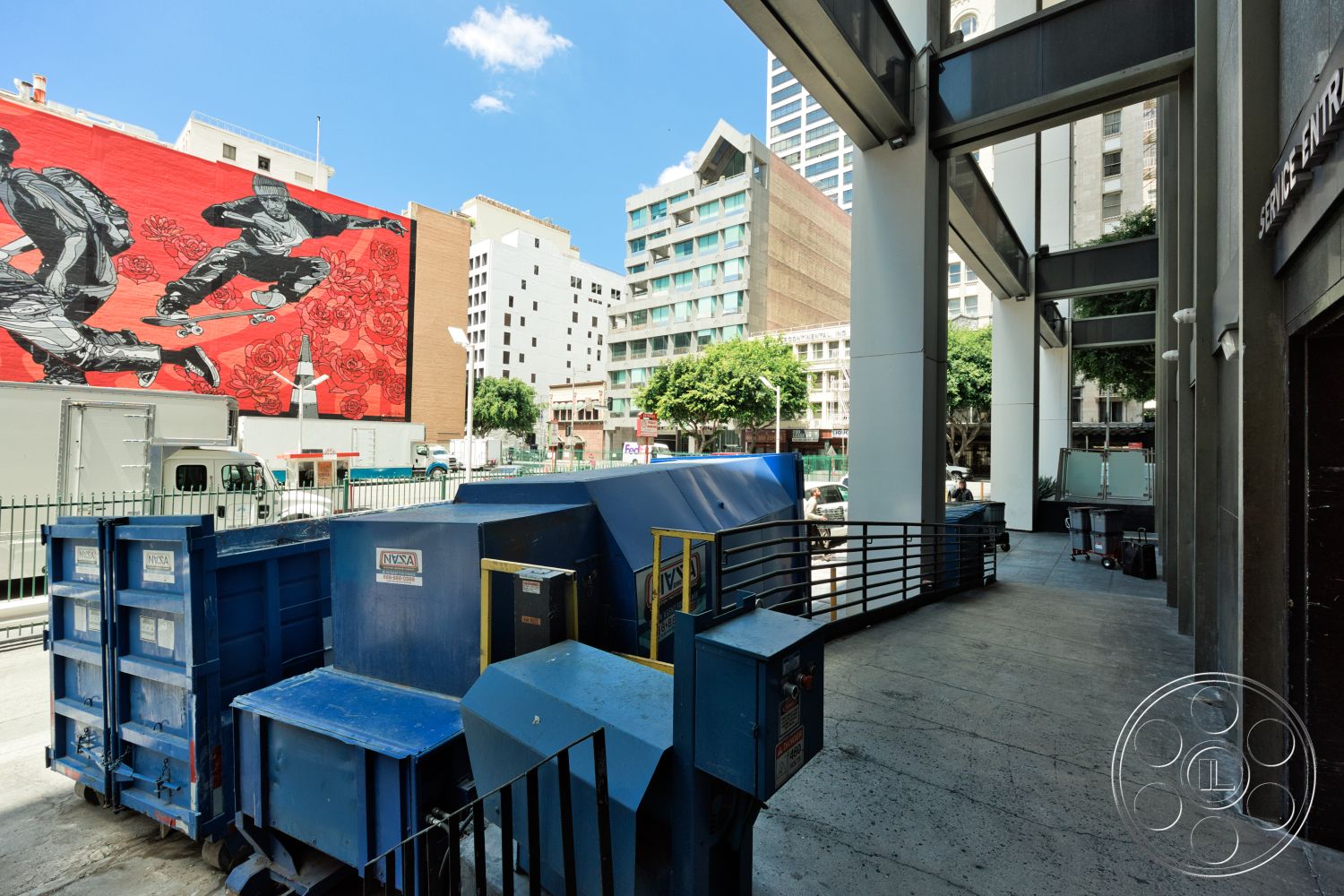 Rooftop 53 - exterior, metal railing, urban landscape, city skyline view, concrete walkway, urban street setting, painted brick mural, industrial dumpster storage, glass and steel building facade, commercial service entrance