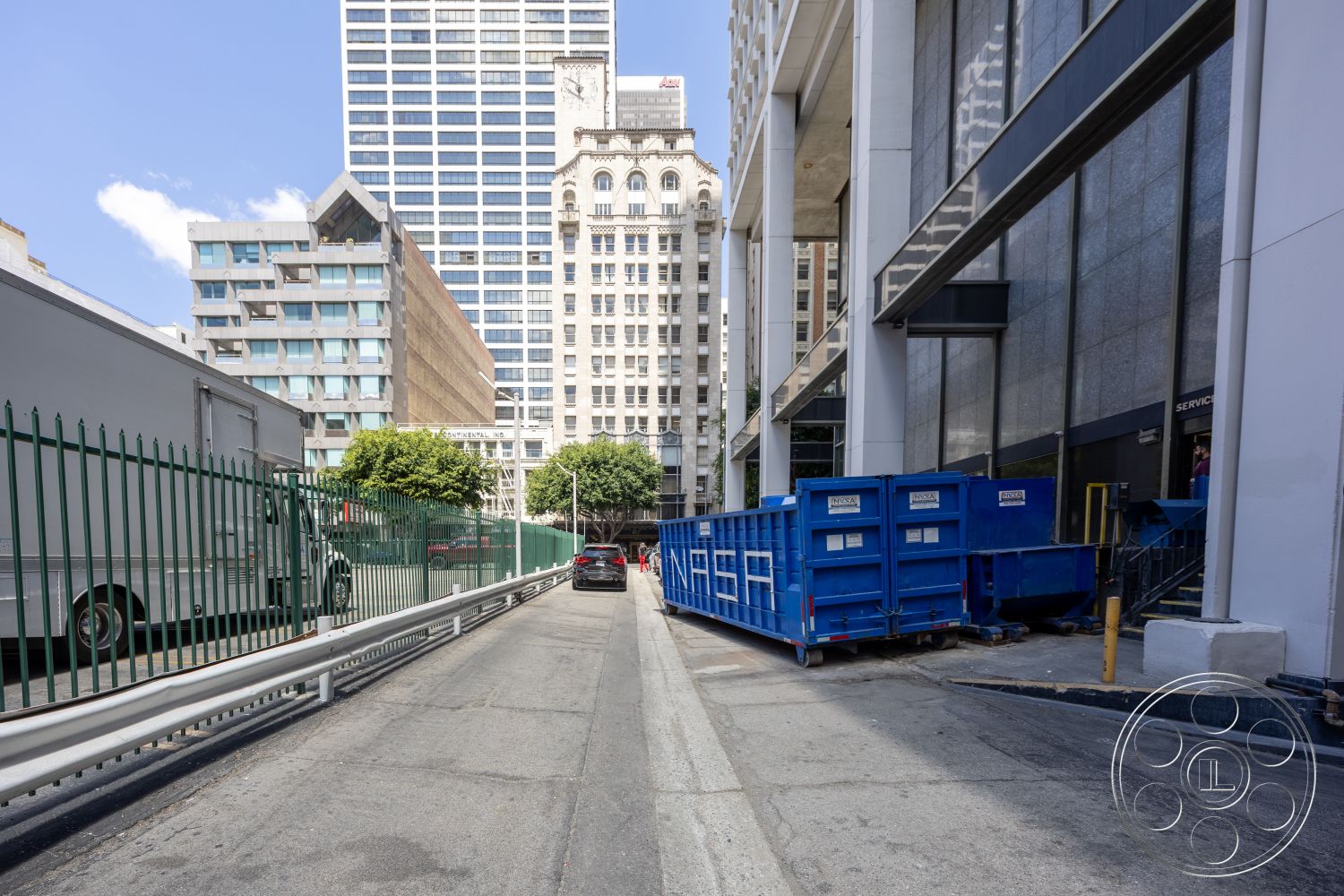 Rooftop 53 - exterior, urban environment, high-rise buildings, concrete sidewalk, surrounding cityscape, steel fence, glass building facade, paved service lane, blue commercial dumpster, mixed-use architecture