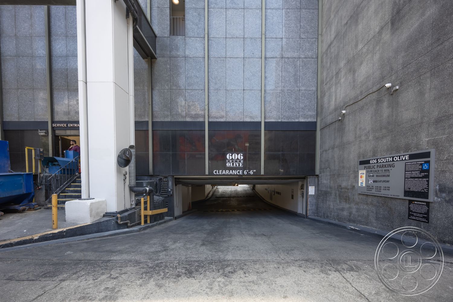 Rooftop 53 - exterior, textured concrete walls, metal railing, smooth concrete ramp, polished concrete driveway, tiled entrance, signage with black background and white text, service entrance with double doors, yellow painted curb barriers, floor-to-ceiling glass at entry, industrial parking area, garage clearance sign