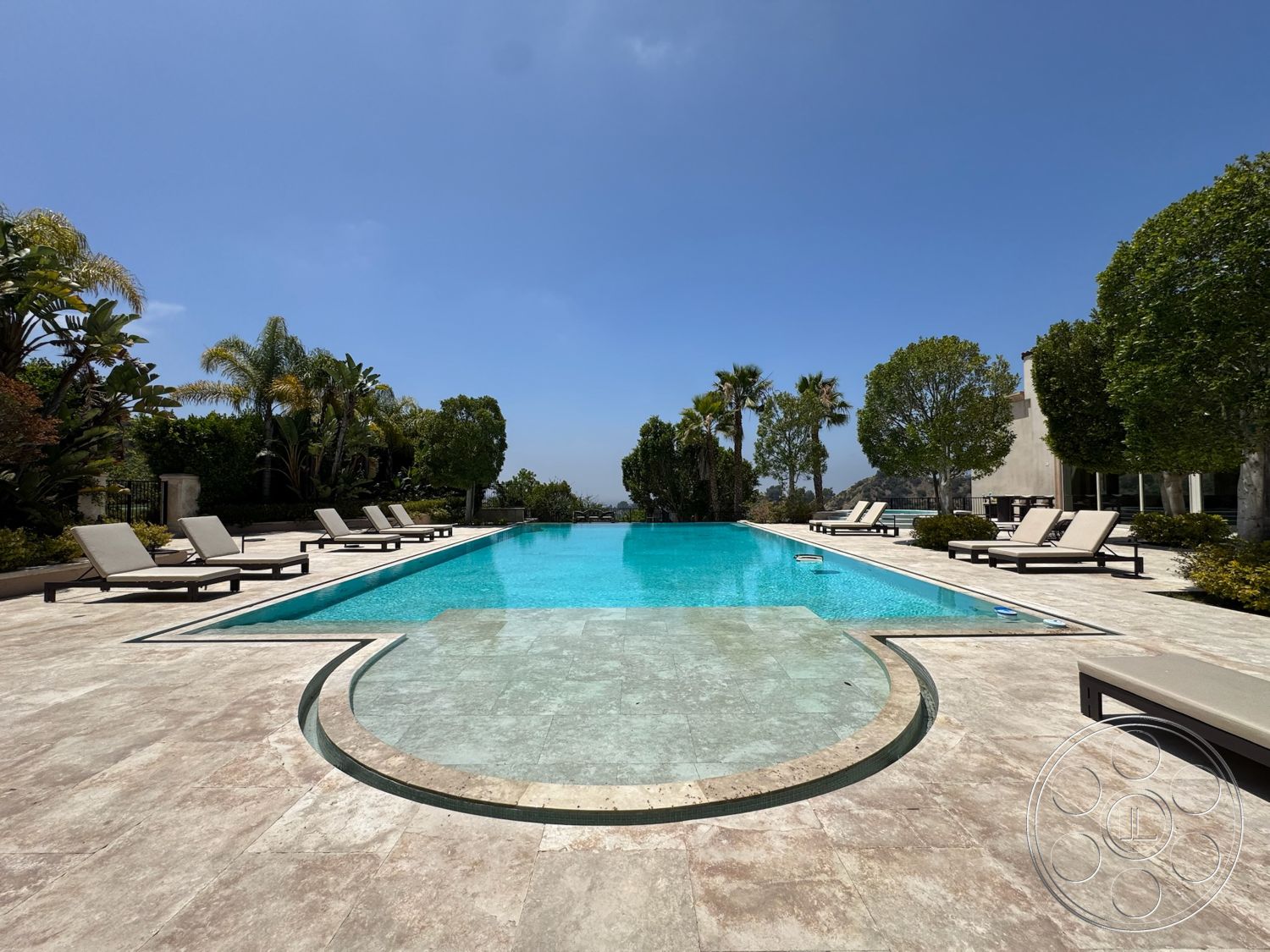 Beverly Compound - exterior, palm trees, outdoor seating area, symmetrical layout, rectangular pool, concrete pool border, natural stone patio flooring, sunny sky backdrop, surrounding tropical landscaping, adjustable lounge chairs, level outdoor space, inviting water surface, fenced properties