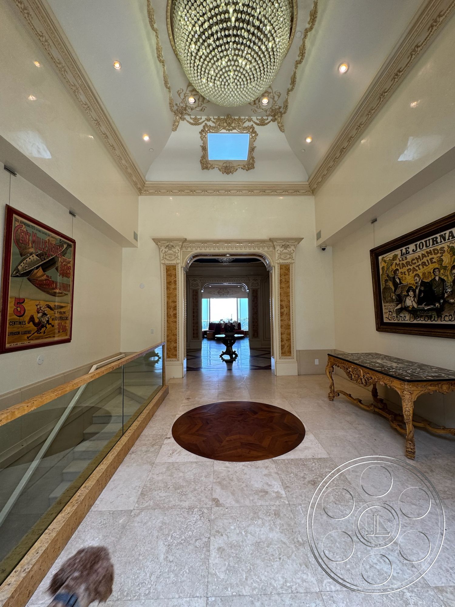 Beverly Compound - dining area view, glass railing, marble flooring, arched entryway, luxurious entrance hall, decorative wall paneling, natural light from skylight, elegant console table, tall ceiling height, herringbone wood inlay, exposed chandelier, intricate ceiling molding, framed vintage posters, ornate doorframe