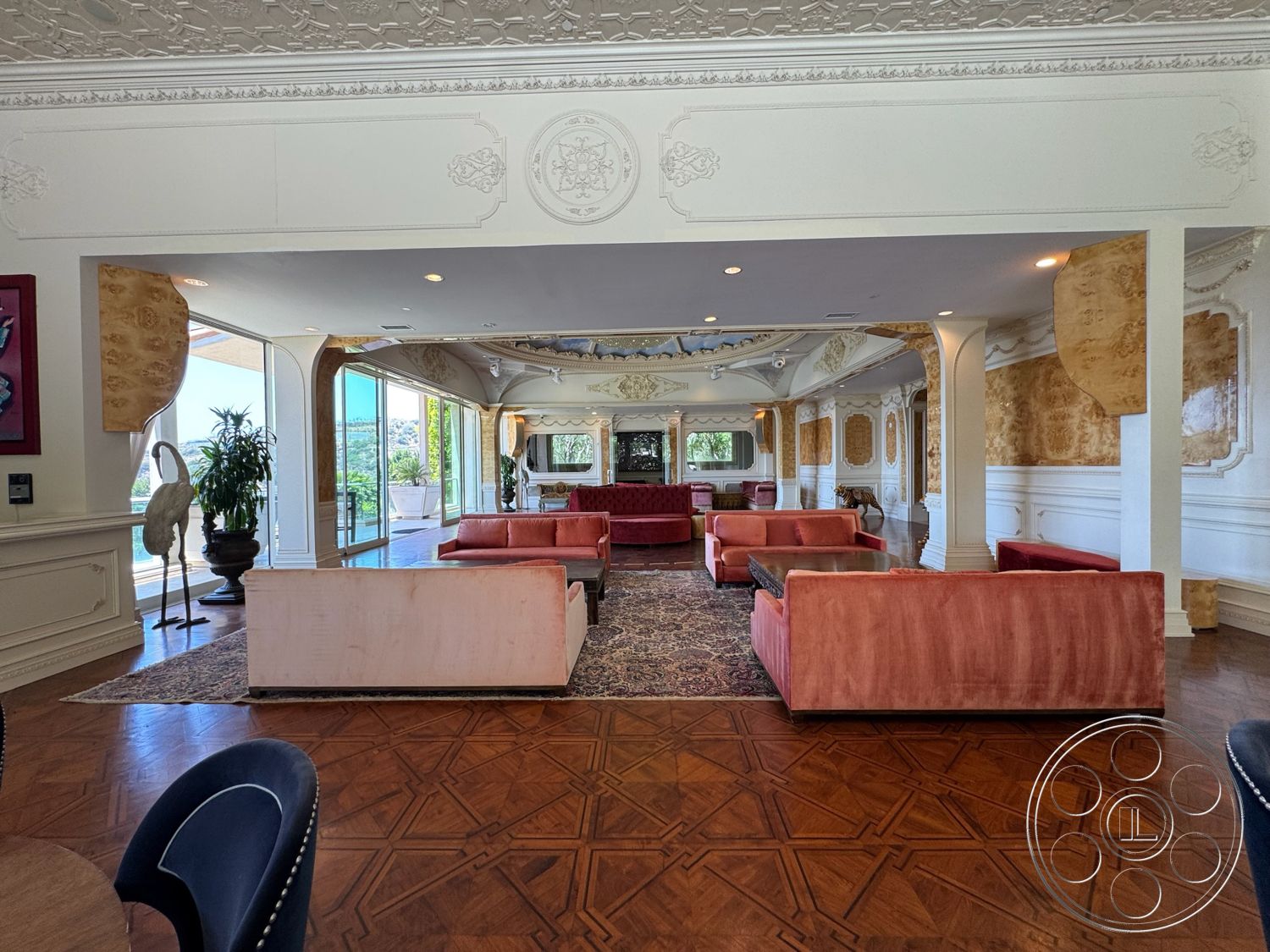 Beverly Compound - open floor plan, dark hardwood flooring, geometric area rug, textured plaster walls, ornate ceiling details, floor-to-ceiling glass sliding doors, natural light-filled living space, decorative wall moldings, wood coffered ceiling, velvet pink sofas, stylish large windows