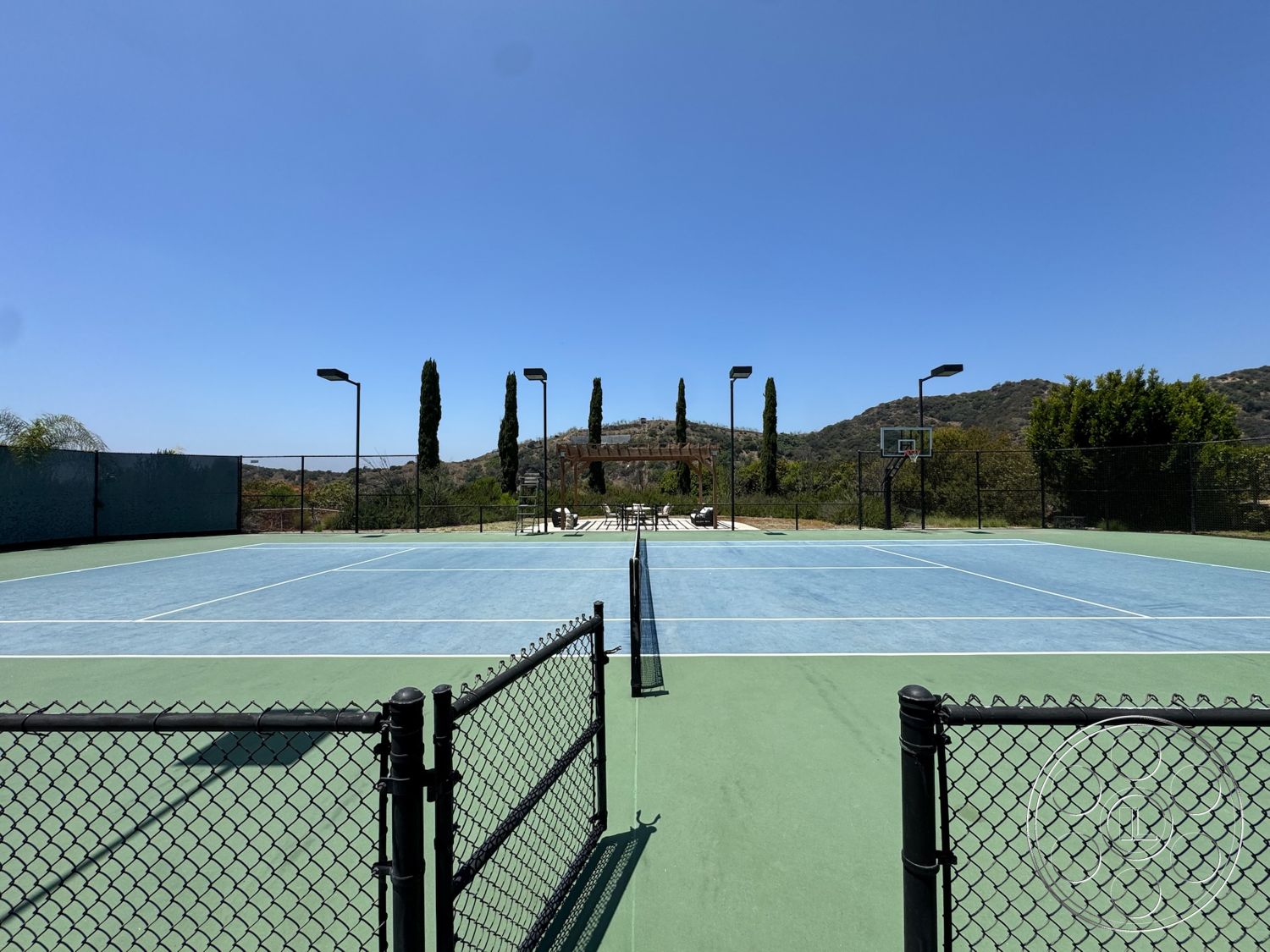 Beverly Compound - exterior, landscaped hillside, mountain view, basketball hoop, tall cypress trees, outdoor lighting fixtures, chain link fence, tennis court surface, asphalt tennis court, blue court lines, relaxation area with chairs