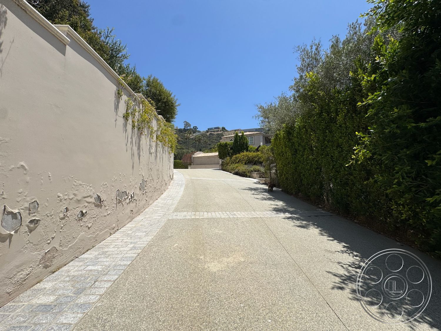 Beverly Compound - exterior, green foliage, curved driveway, gravel driveway, residential setting, landscaped hedges, plaster wall, sunny hillside location, paved stone border, decorative stone pathway