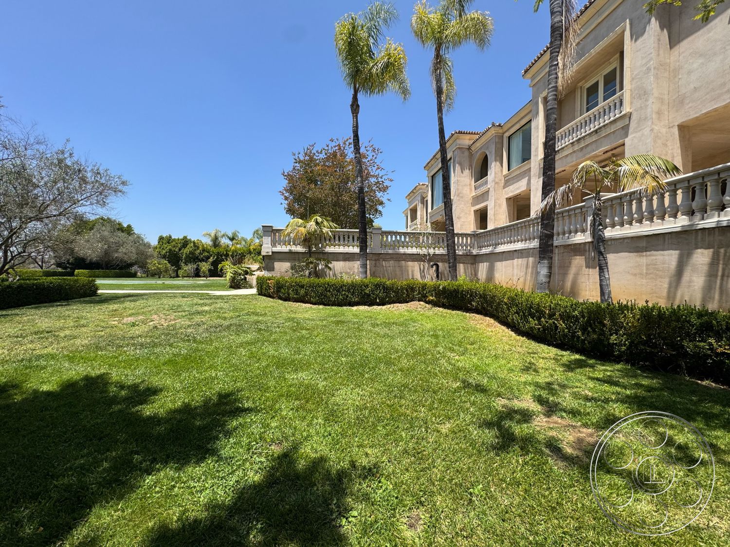 Beverly Compound - exterior, palm trees, curved pathway, landscaped lawn, residential backyard, two-story building, grassy terrain, sunny outdoor setting, hedge border, stucco wall finish, balustrade railing, arched window features