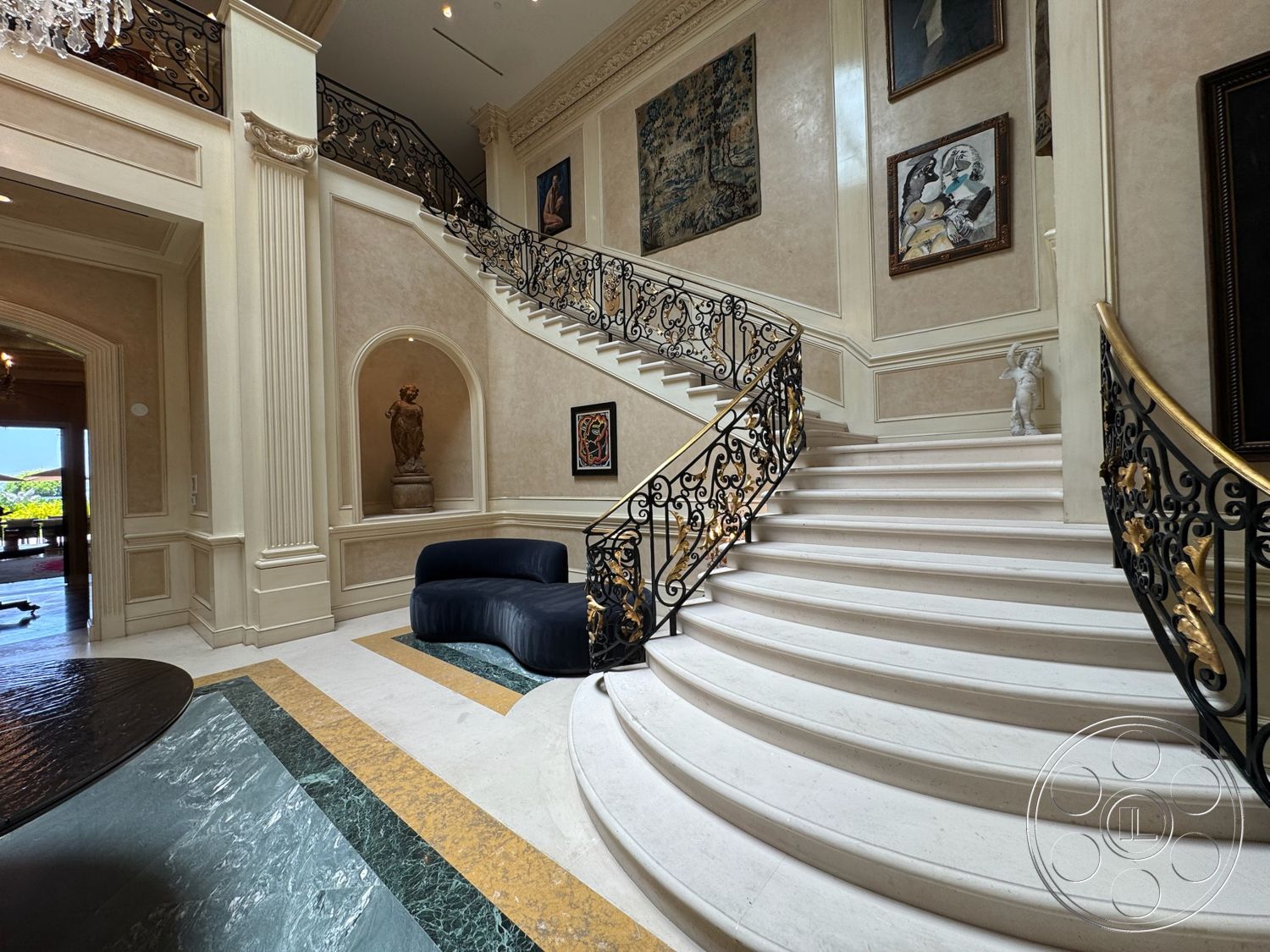 Beverly Compound - polished marble flooring, textured plaster walls, arched entryway, exposed wood ceiling beams, coffered ceiling details, framed artwork on walls, intricate wrought iron railing, marble staircase, statue decor, luxurious entry hallway