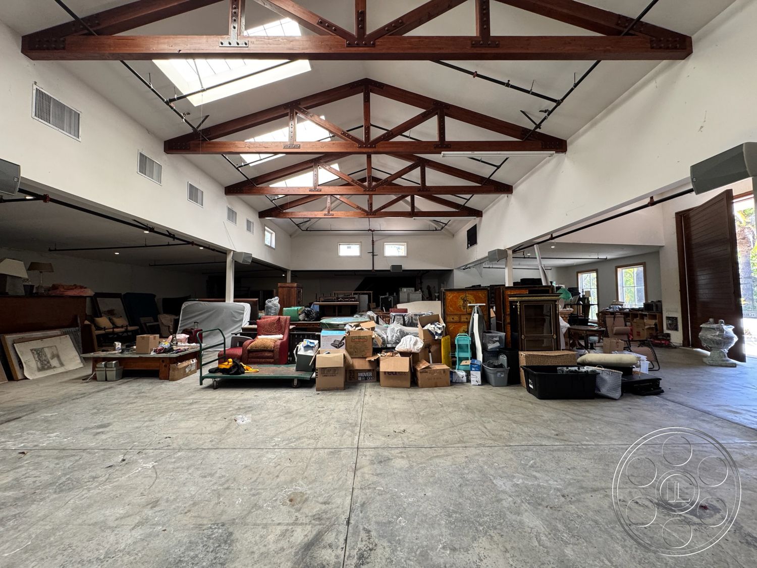Beverly Compound - large windows, open floor plan, polished concrete flooring, vaulted ceiling, skylights, white plaster walls, exposed wood ceiling beams, natural light throughout, industrial style interior, built-in storage units, warehouse-style architecture, rural loft setting