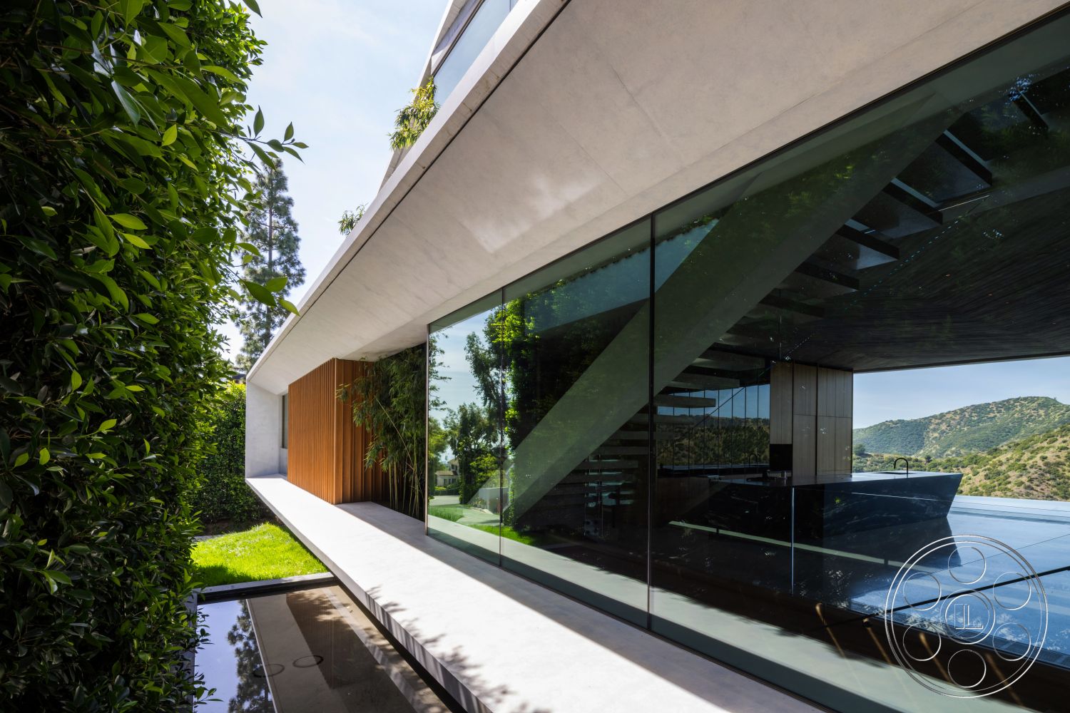 Modern 516 - exterior, minimalist style, glass railings, open outdoor space, flat roof design, landscaped garden area, floor-to-ceiling glass windows, modern architectural design, steel structural elements, sloped hillside location, rectangular concrete patio, concrete overhang, wood accent paneling, greenery surrounding building
