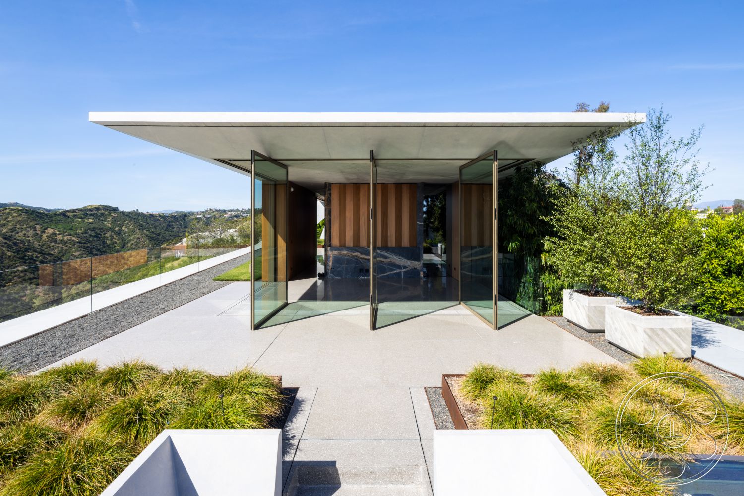 Modern 516 - exterior, modern architecture, glass sliding doors, mountain view, minimalist landscaping, concrete flat roof, green grass landscaping, rectangular concrete planters, polished concrete patio flooring, wood paneling entrance wall, horizontal glass railing, sloping site