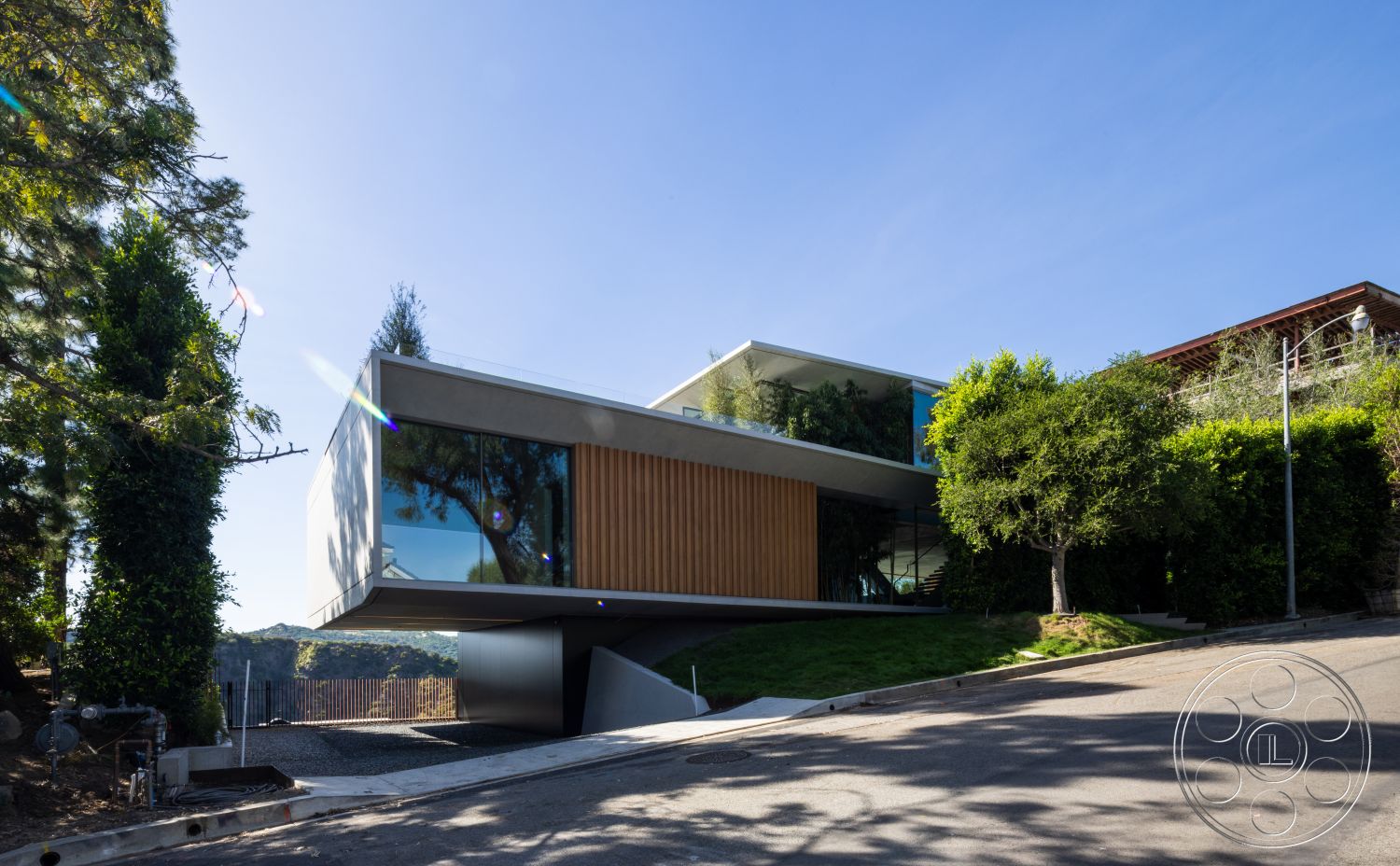 Modern 516 - exterior, flat roof, large glass windows, concrete walls, wood paneling accents, modern hillside home, landscaped garden with trees, sloping driveway, angular architectural design, linear exterior shape