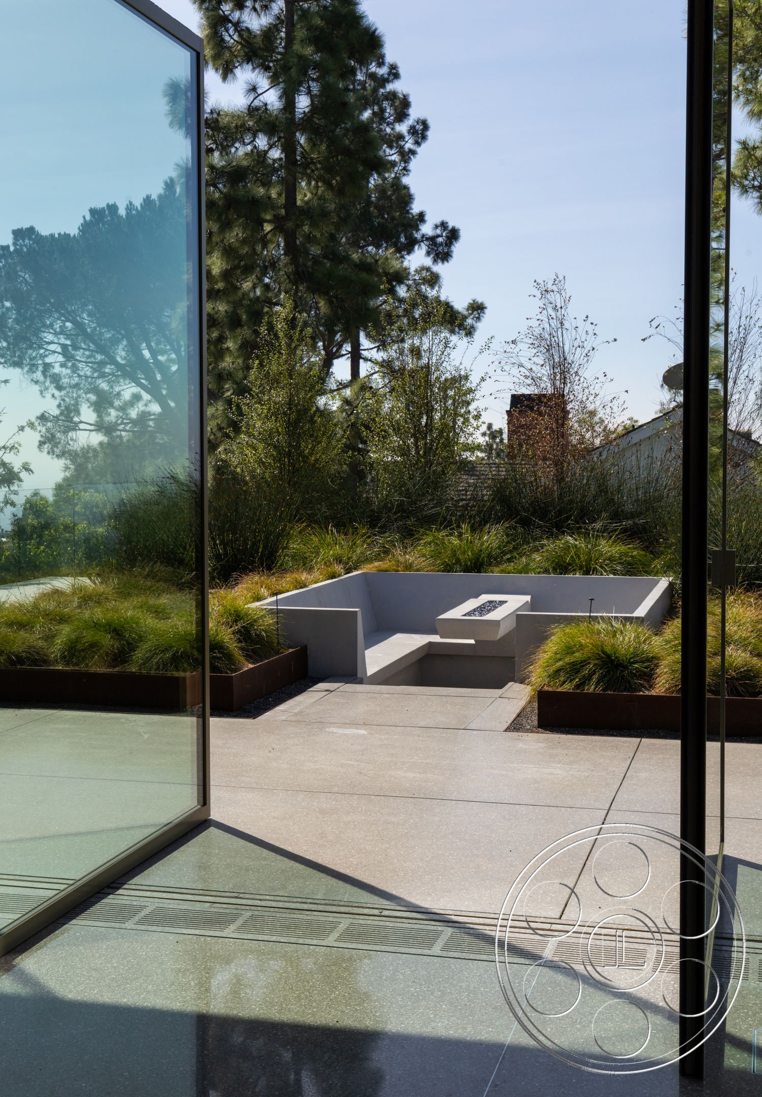 Modern 516 - exterior, modern architectural style, clear sky view, landscaped garden area, concrete patio flooring, floor-to-ceiling glass walls, rectangular fire pit, metal planter boxes, grassy landscaping, trees in the background