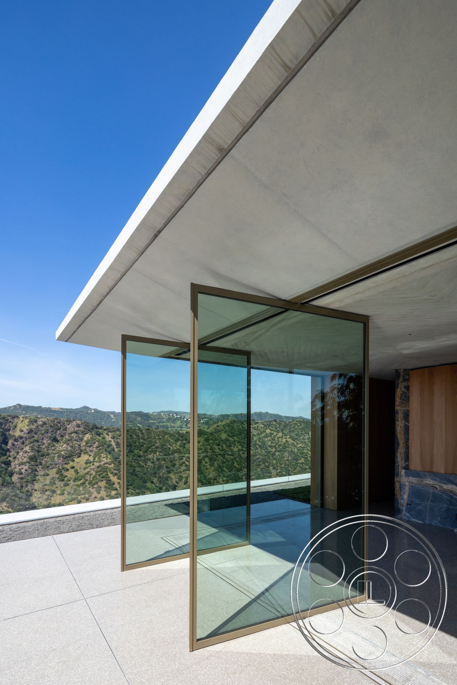 Modern 516 - exterior, polished concrete flooring, glass sliding doors, mountain view, open-air patio, landscape integration, minimalist architectural style, concrete overhang, bronze frame details, clear glass panels, vertical glass surfaces