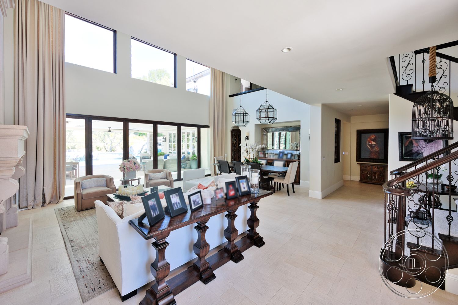 Hayden House - high ceilings, large windows, natural lighting, stone fireplace, textured area rug, open floor plan, decorative vases, white upholstered sofa, light-colored tile flooring, neutral wall paint, dark wood accent table, black metal stair railing, decorative wall mirrors, hanging lantern light fixtures, cream-colored linen drapes, dining area with wooden dining table