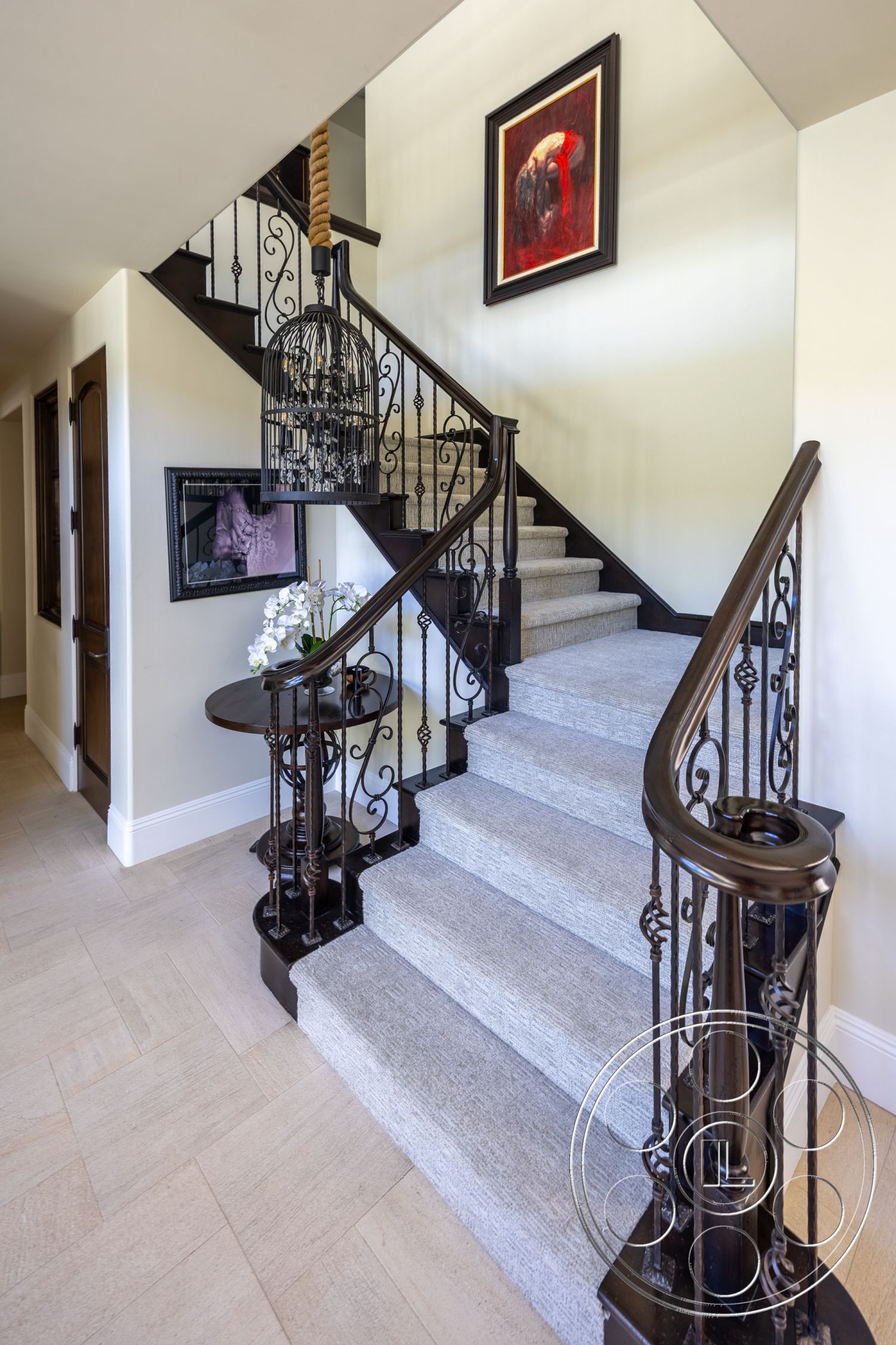 Hayden House - framed wall art, black wrought iron railings, curved staircase, light beige wall paint, carpeted staircase, wood landing table, tile floor with herringbone pattern, vintage-style hanging light fixture