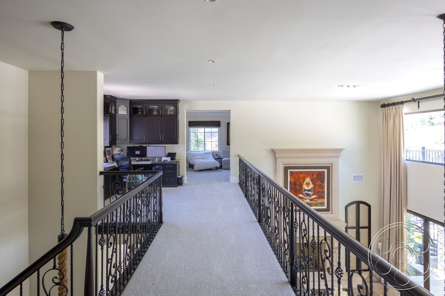 Hayden House - floor-to-ceiling windows, open concept living space, stone fireplace surround, carpeted hallway flooring, light beige painted walls, iron railing with decorative scrollwork, built-in dark wood office cabinetry, wall-mounted decorative artwork, neutral-colored drapery