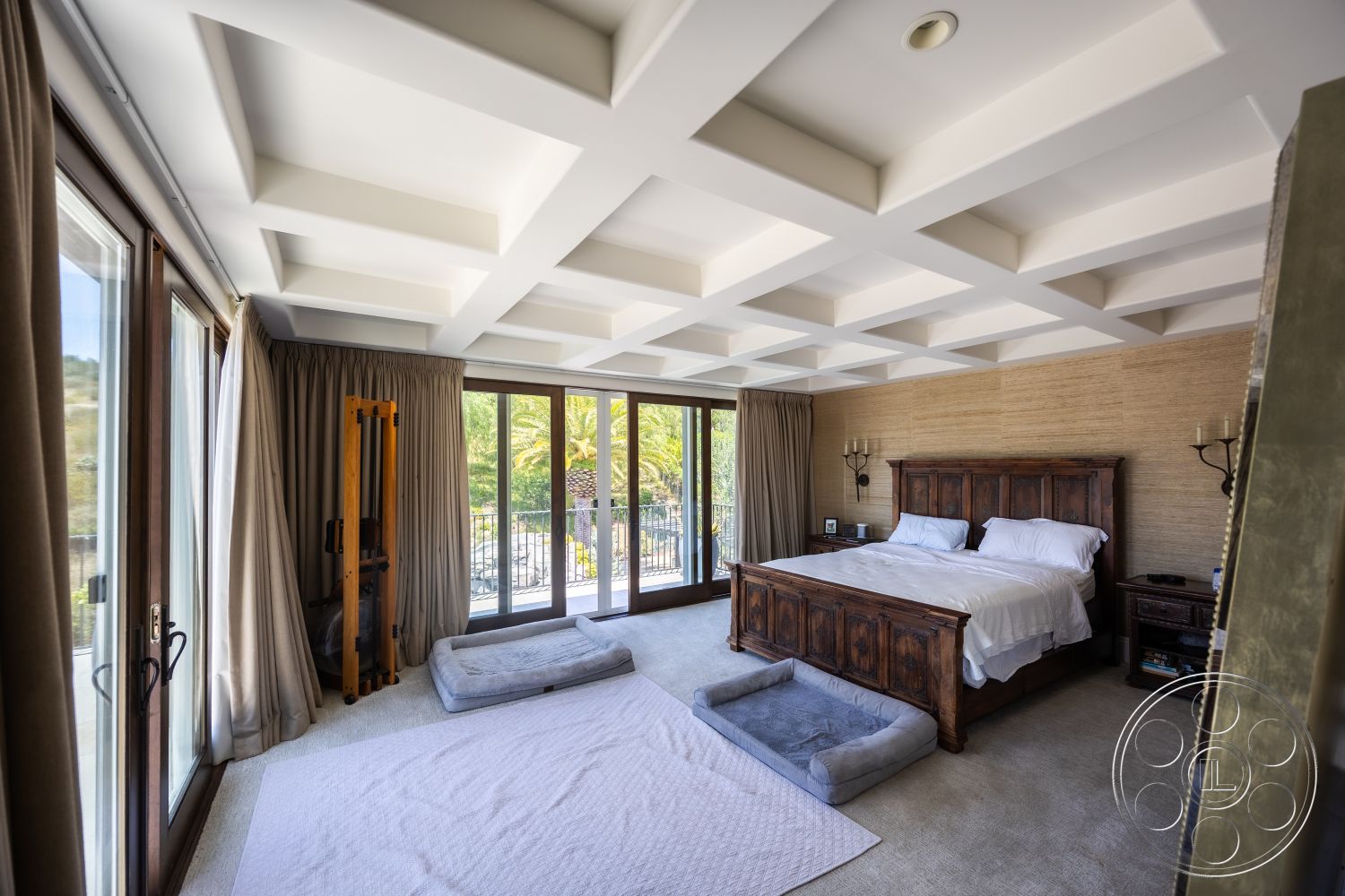 Hayden House - coffered ceiling, floor-to-ceiling windows, wooden bed frame, textured wall treatment, wooden nightstands, luxurious bedding, curtained windows, carpet bedroom flooring, elegant wall sconces