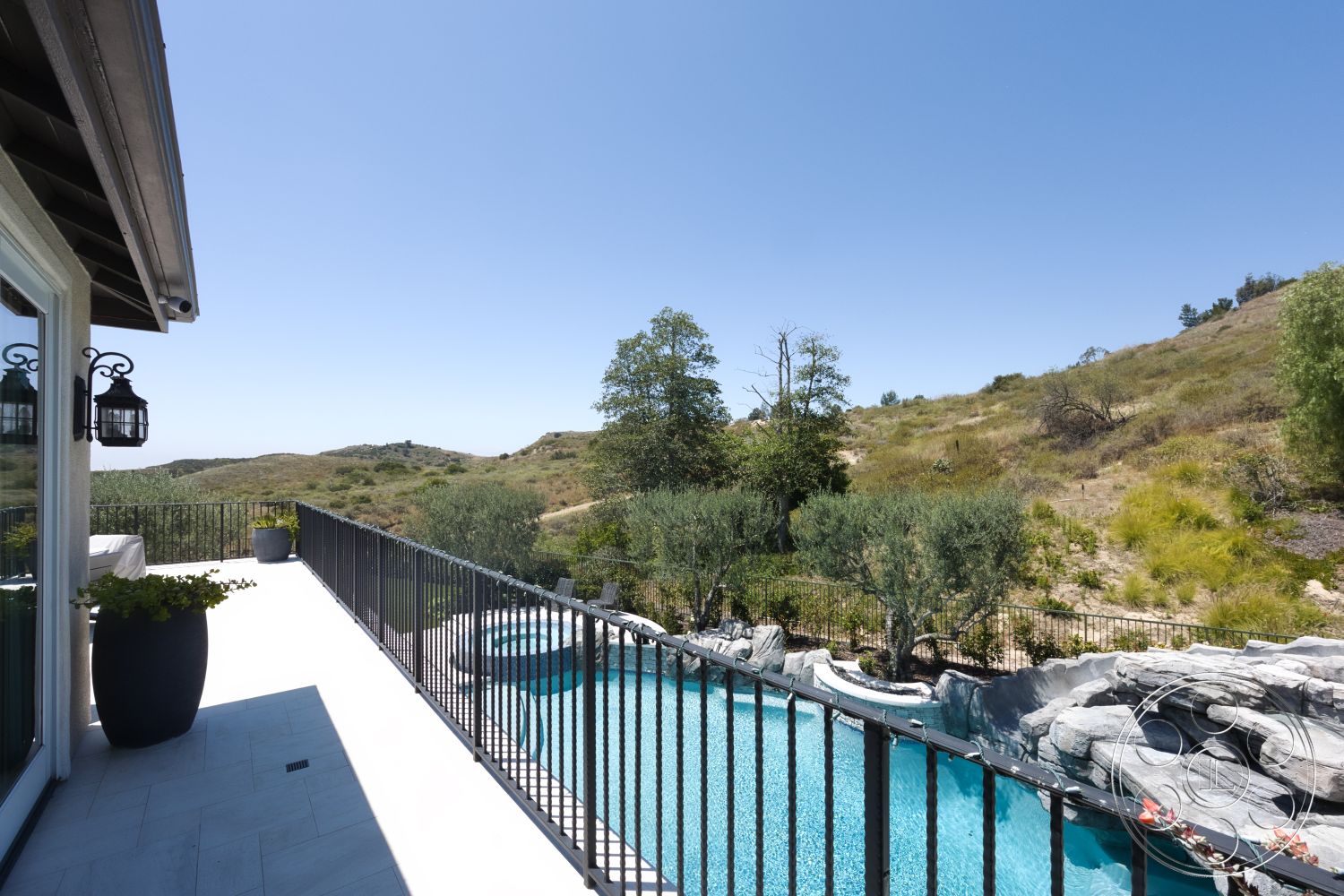 Hayden House - glass sliding doors, black metal railing, rectangular pool, planter pots, outdoor lighting fixtures, sunny exterior, mountain view setting, landscaped garden area, concrete patio flooring, natural stone pool border
