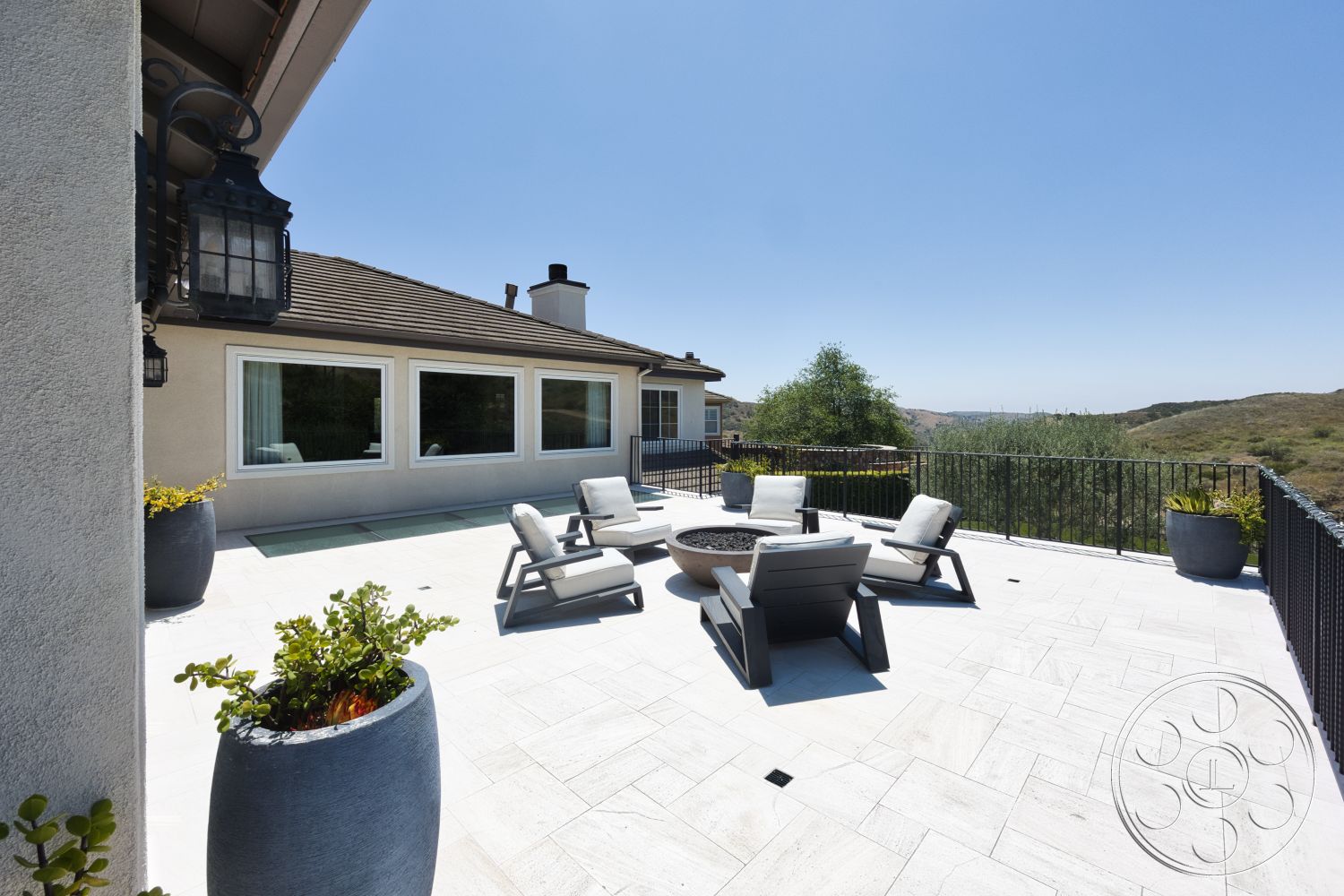 Hayden House - exterior, landscaped garden, floor-to-ceiling windows, black metal railing, gray stucco exterior, sunny outdoor setting, flat roof design, modern outdoor seating area, stone patio flooring, concrete planter pots, sloped hillside view, dark wood roof shingles, built-in fire pit