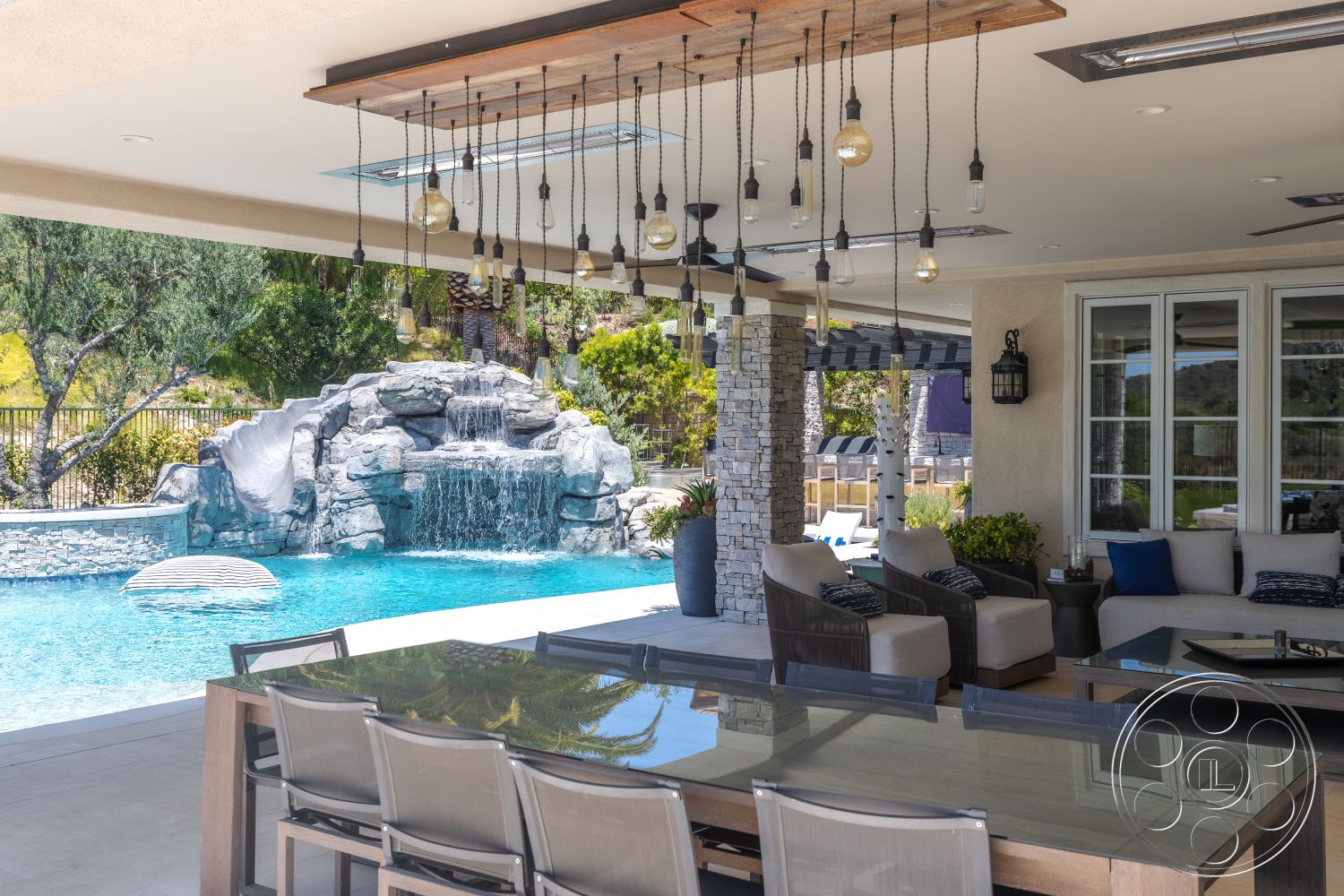 Hayden House - exterior, glass sliding doors, rectangular swimming pool, landscaped backyard, concrete patio flooring, wood ceiling details, stone column details, natural stone waterfall, hanging industrial light fixtures, fiber patio dining chairs, pool area with slide, outdoor kitchen dining area
