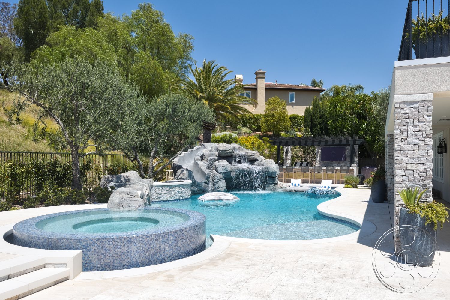 Hayden House - exterior, surrounding greenery, circular spa, lush garden landscaping, stucco home exterior, paved patio flooring, wood trellis structure, oval pool with mosaic tile border, natural stone waterfall feature, textured stone pool decking