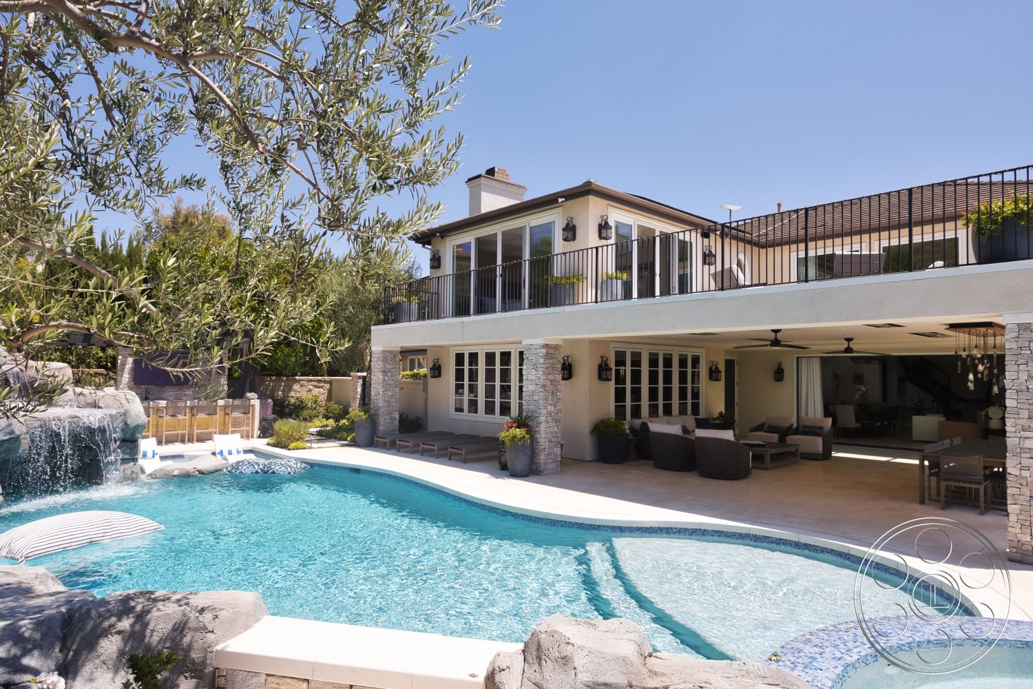 Hayden House - exterior, floor-to-ceiling windows, concrete pool deck, sloping roofline, metal balcony railing, paved outdoor seating area, decorative outdoor lighting fixtures, landscaped garden with greenery, stacked stone wall, kidney-shaped pool, stone waterfall feature, patio seating area with outdoor furniture, weathered wood ceiling