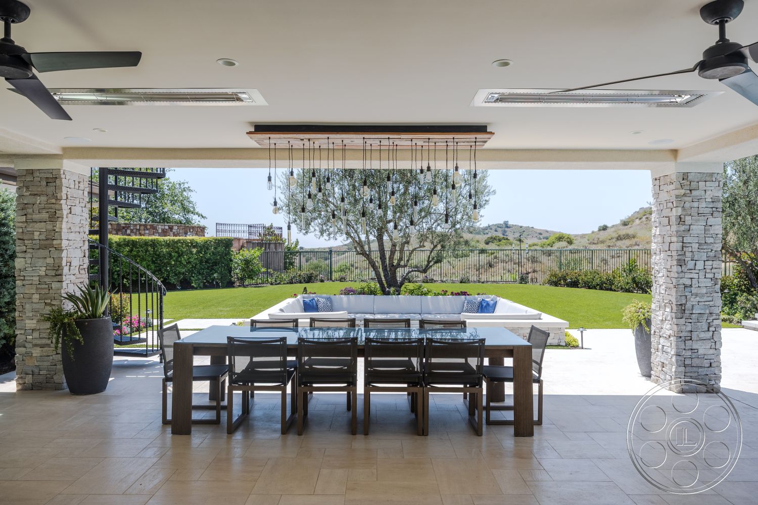 Hayden House - exterior, potted plants, outdoor seating area, glass railing, modern aesthetic, spiral staircase, landscaped backyard, lush green grass, hillside view, wooden dining chairs, pendant lighting fixtures, concrete patio flooring, open patio space, stone accent walls, stainless steel outdoor dining table, outdoor ceiling fans
