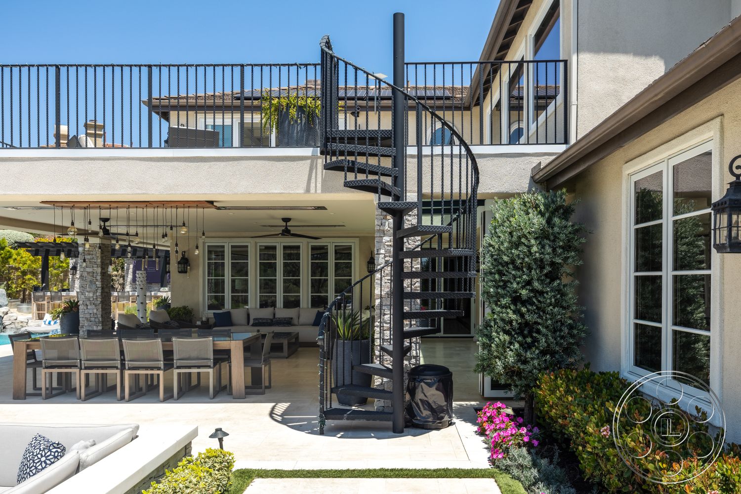 Hayden House - exterior, modern residential architecture, stucco wall finish, tile patio flooring, glass window wall, covered patio area, pool area with lounge chairs, stone column supports, spiral metal staircase, horizontal wood patio dining table, hanging outdoor pendant lights, landscaped garden with flowering shrubs, suspended wood ceiling beams
