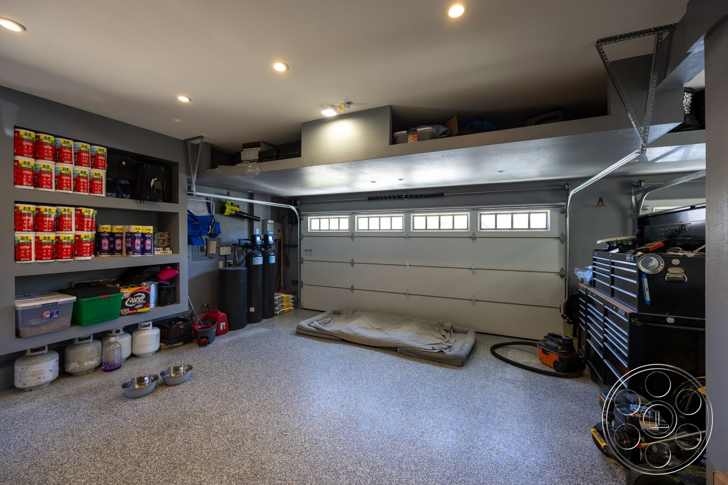 Hayden House - fluorescent ceiling lights, gray painted walls, interior garage space, epoxy flooring, overhead garage door, ceiling-mounted storage racks, tool storage chest, shelving units for organizational storage