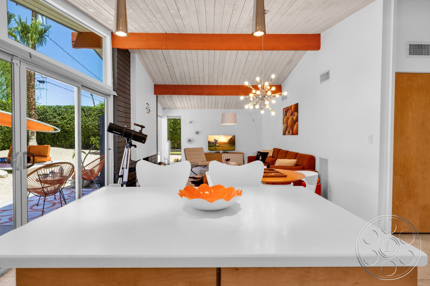 Palm Springs 76 - modern light fixtures, concrete flooring, glass sliding doors, floor-to-ceiling windows, open-concept living space, mid-century modern style, wood beam ceiling, white painted walls, built-in entertainment unit, orange upholstery sofa, acrylic dining chairs, decorative fruit artwork