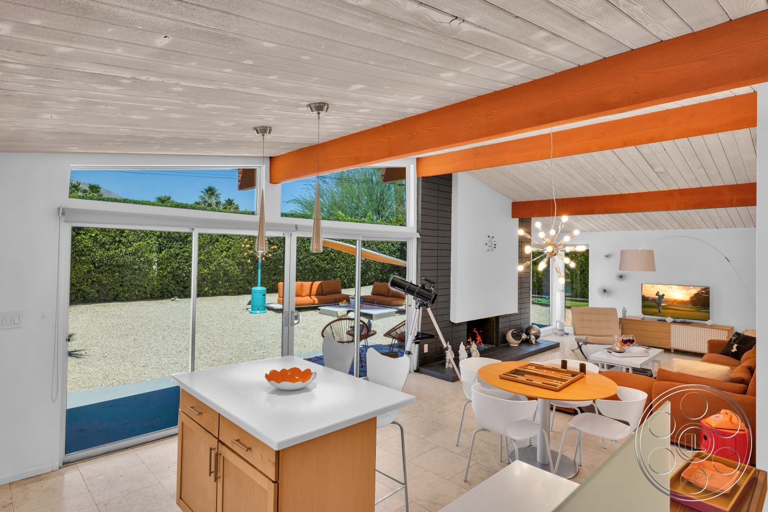 Palm Springs 76 - open floor plan, glass sliding doors, natural stone flooring, outdoor view, white kitchen island, pendant lighting fixtures, modern dining area, exposed wood ceiling beams, orange sectional sofa, white painted walls, modern architectural design, gravel patio area, black stone fireplace surround, rounded accent chair, maple cabinetry