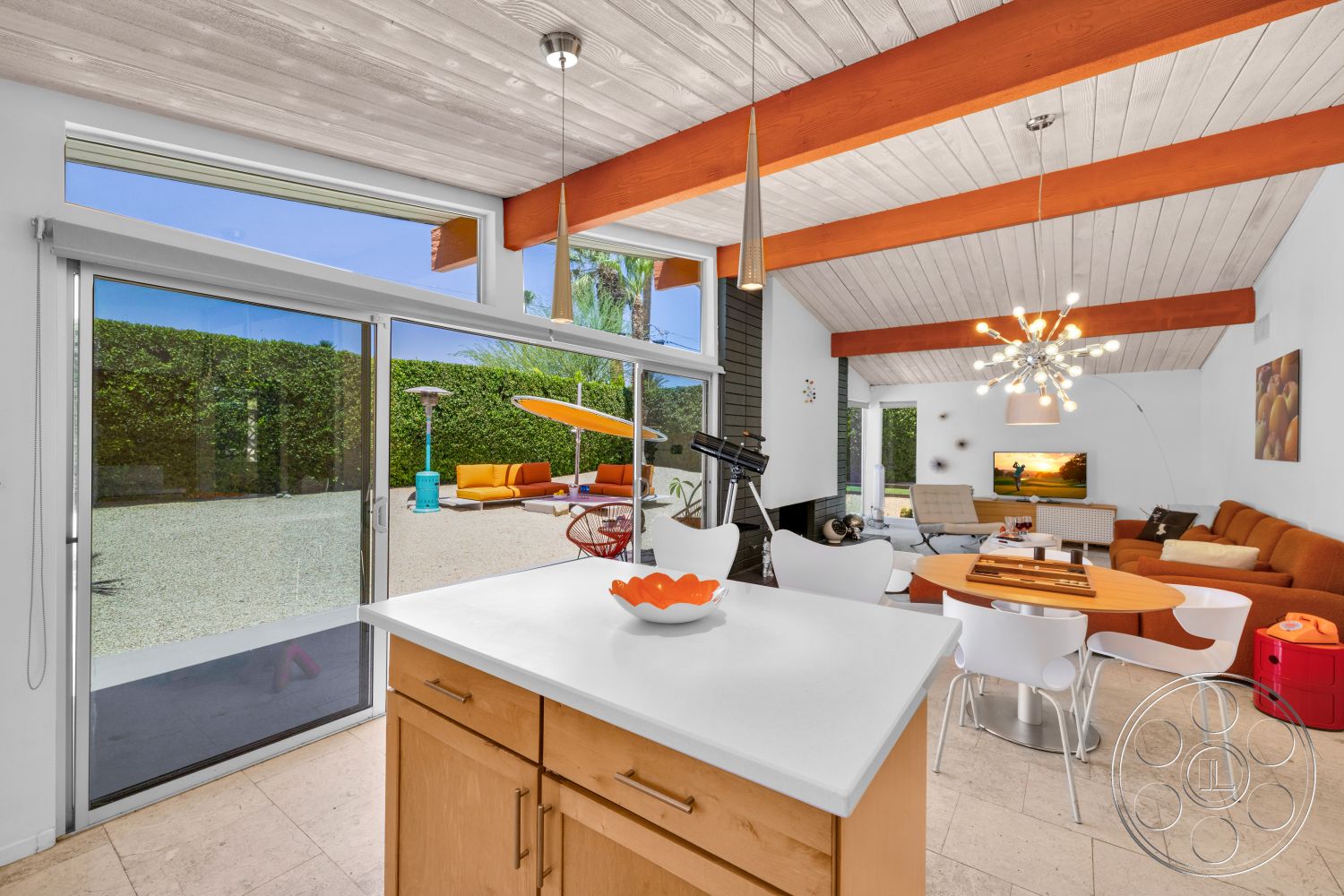 Palm Springs 76 - modern pendant lighting, glass sliding doors, garden view, round dining table, flat-screen TV, slate tile flooring, textured sofa, wood beam ceiling, white painted walls, open concept living area, vaulted living room ceiling, modern accent chairs, light wood kitchen cabinets, solid surface kitchen countertops