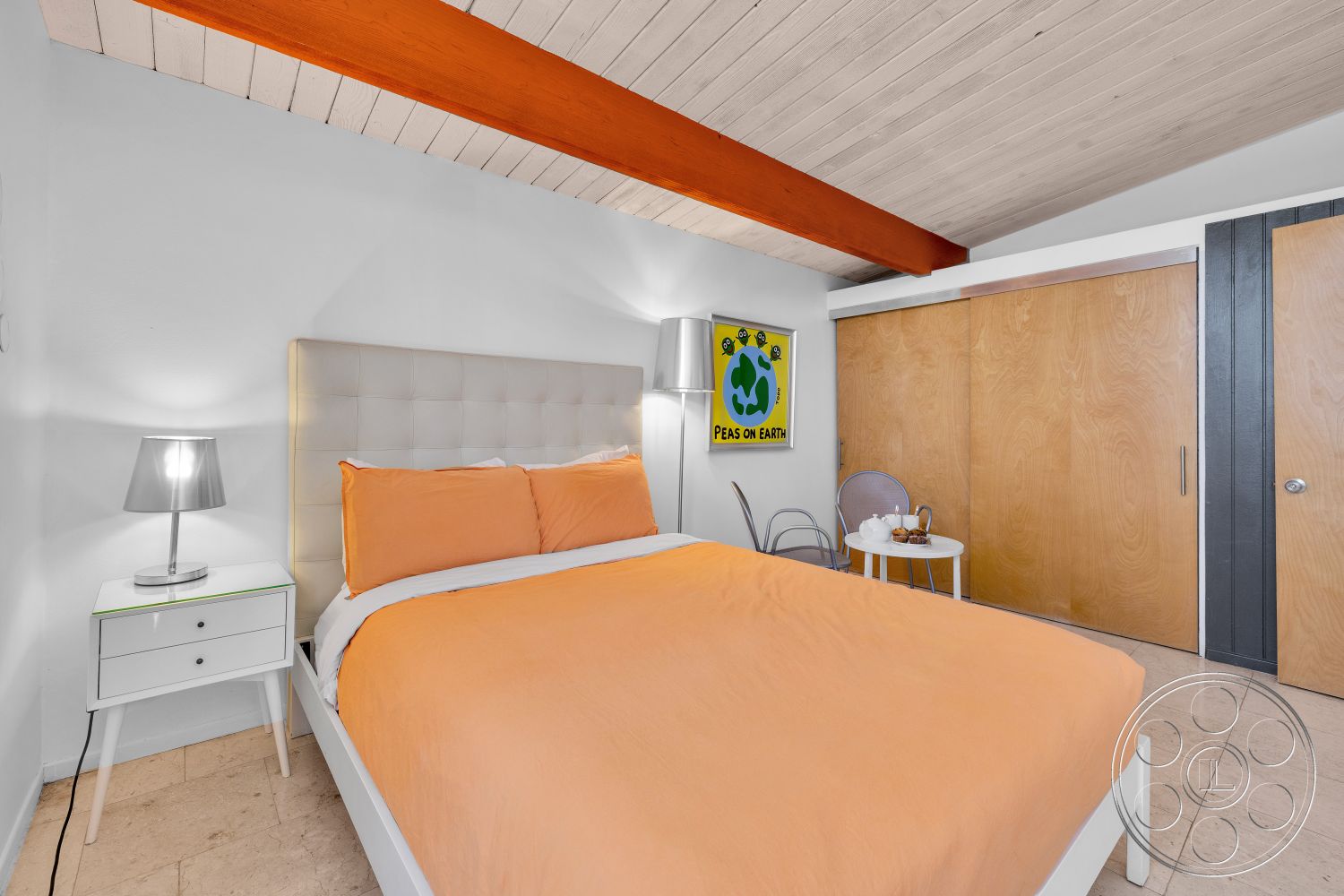 Palm Springs 76 - artwork on wall, exposed wood ceiling beams, white painted walls, tile bedroom flooring, modern bedside lamp, minimalist side table, simple dining chair, quilted headboard, orange bed linens, sliding wood closet doors, colored wall art