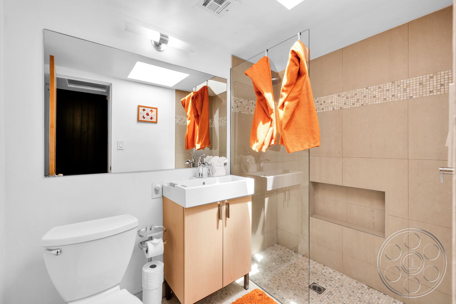 Palm Springs 76 - glass shower enclosure, rectangular mirror, chrome faucet, wall-mounted light fixture, white painted walls, tile bathroom walls, floating bathroom vanity, mosaic tile accent strip, pebble stone shower floor, orange bathroom towels, toilet with curved design