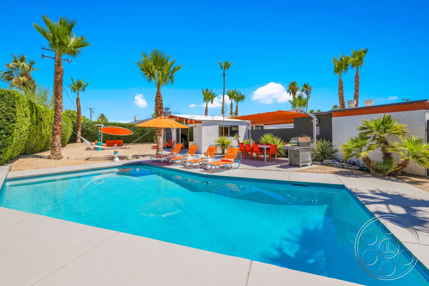 Palm Springs 76 - exterior, white stucco walls, flat roof, palm trees, glass sliding doors, modern outdoor furniture, desert landscaping, concrete pool deck, rectangular pool, gravel ground cover, concrete patio flooring, open outdoor dining area, orange patio umbrellas, colorful accent seating