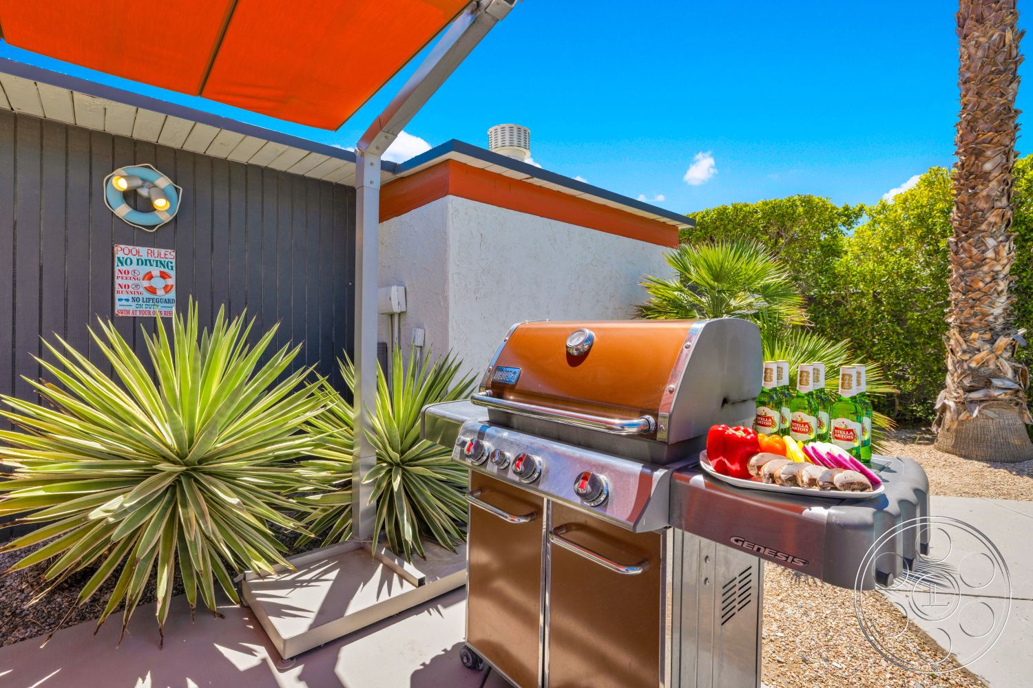 Palm Springs 76 - exterior, desert plants, functional outdoor space, safety sign, stucco exterior walls, flat roof structure, concrete patio floor, outdoor grilling area, stainless steel gas grill, orange retractable awning, desert landscaping with palm trees