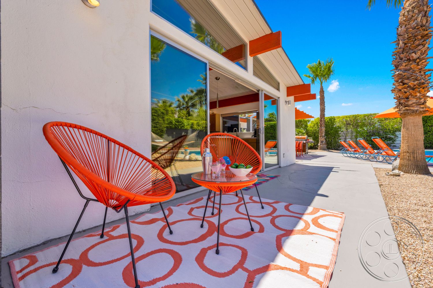 Palm Springs 76 - decorative area rug, exterior, landscaped garden, modern architecture, open concept layout, floor-to-ceiling windows, outdoor dining area, poolside lounge chairs, textured wall treatment, sunshade umbrellas, orange accent chairs, flat roof design, concrete patio floor, palm tree surroundings