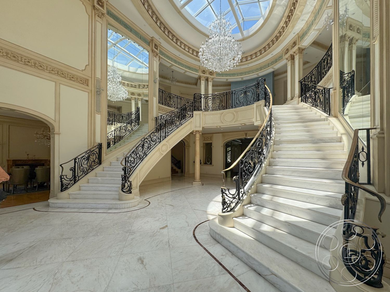 Tiffany Estate - marble flooring, black wrought iron railings, ornate ceiling details, large reflective mirrors, chandelier lighting fixture, vaulted ceiling with skylight, curved marble staircase, elegant foyer space, elaborate crown molding