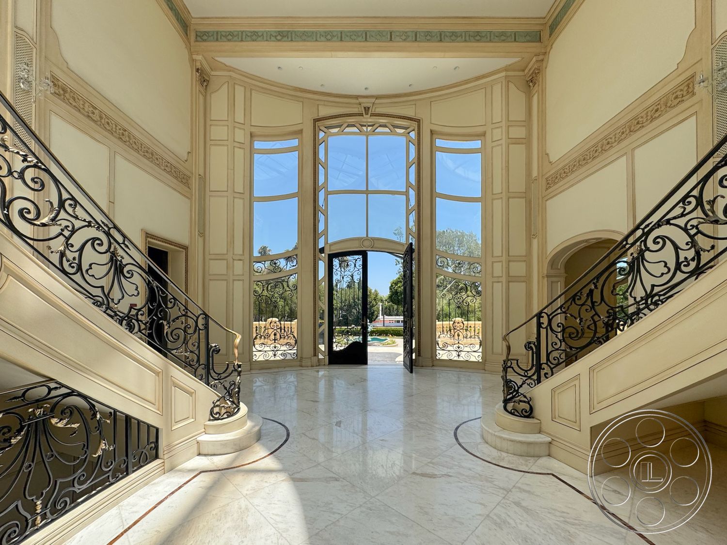 Tiffany Estate - natural light, open floor plan, vaulted ceiling, marble flooring, arched doorways, large floor-to-ceiling windows, double front doors, curved staircase, black wrought iron railing, elegant foyer, ornate wall molding, light beige wall paneling, decorative ceiling trim, expansive entryway